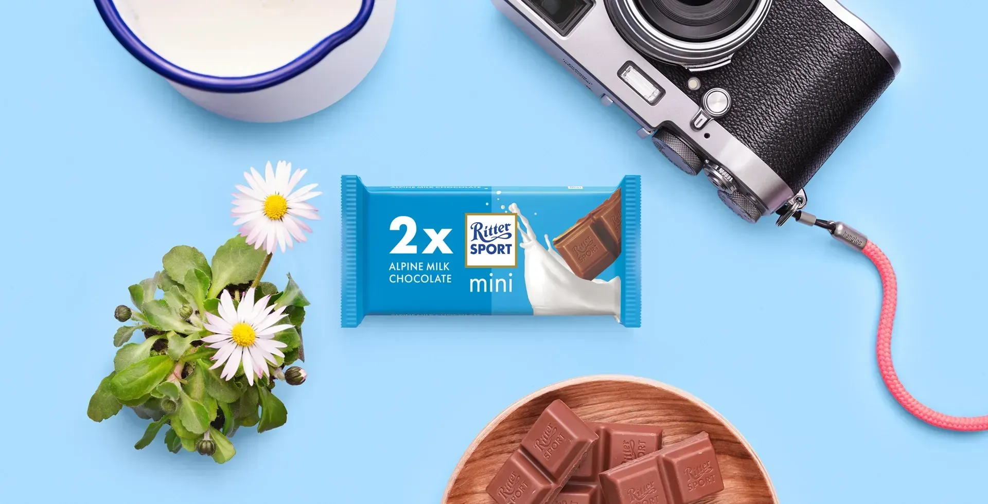 Ritter Sport chocolate bar packaging with cocoa beans, broken chocolate, and milk on a blue background.