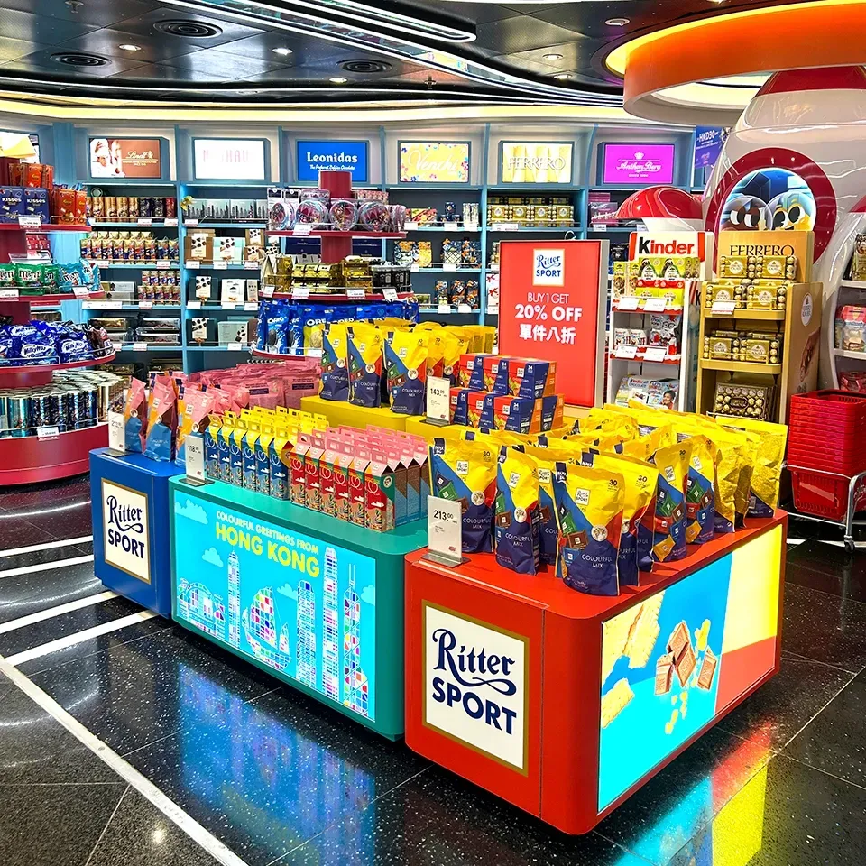 Display of Ritter Sport chocolate in a brightly lit duty-free shop; colorful boxes and shelves.