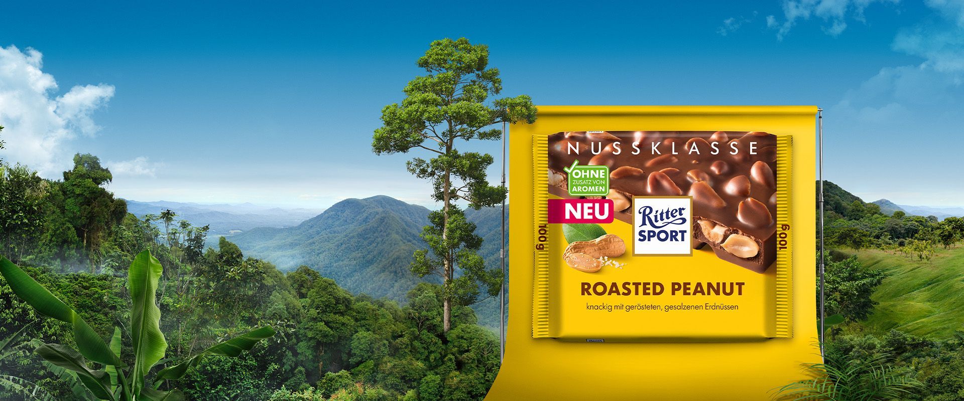 Werbung für einen Schokoriegel in einer Landschaft mit grünen Bäumen und blauem Himmel.