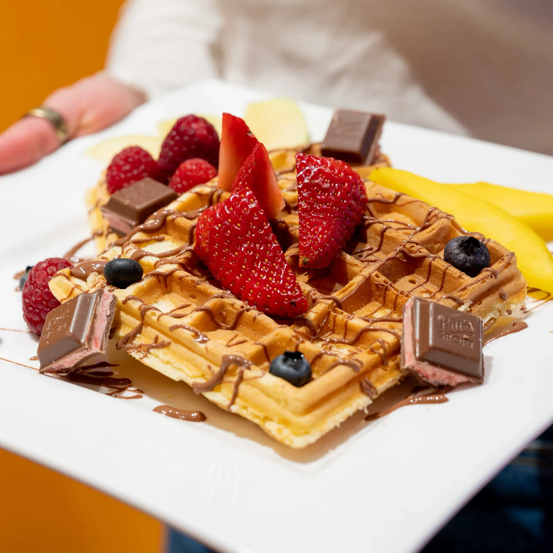 Eine Person hält einen Teller mit Waffeln mit Erdbeeren und Blaubeeren obenauf