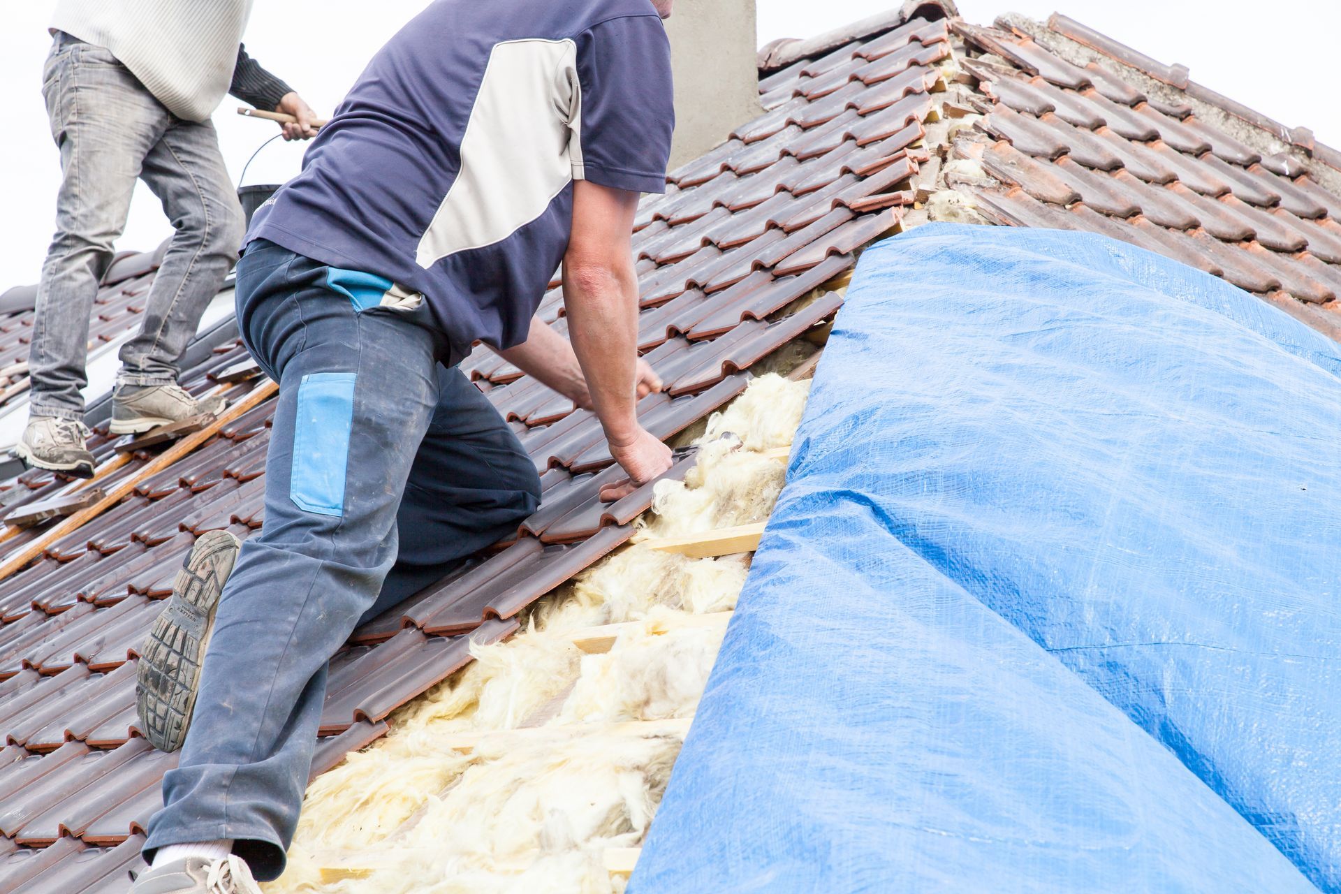 Two men are working on a roof with a blue tarp.