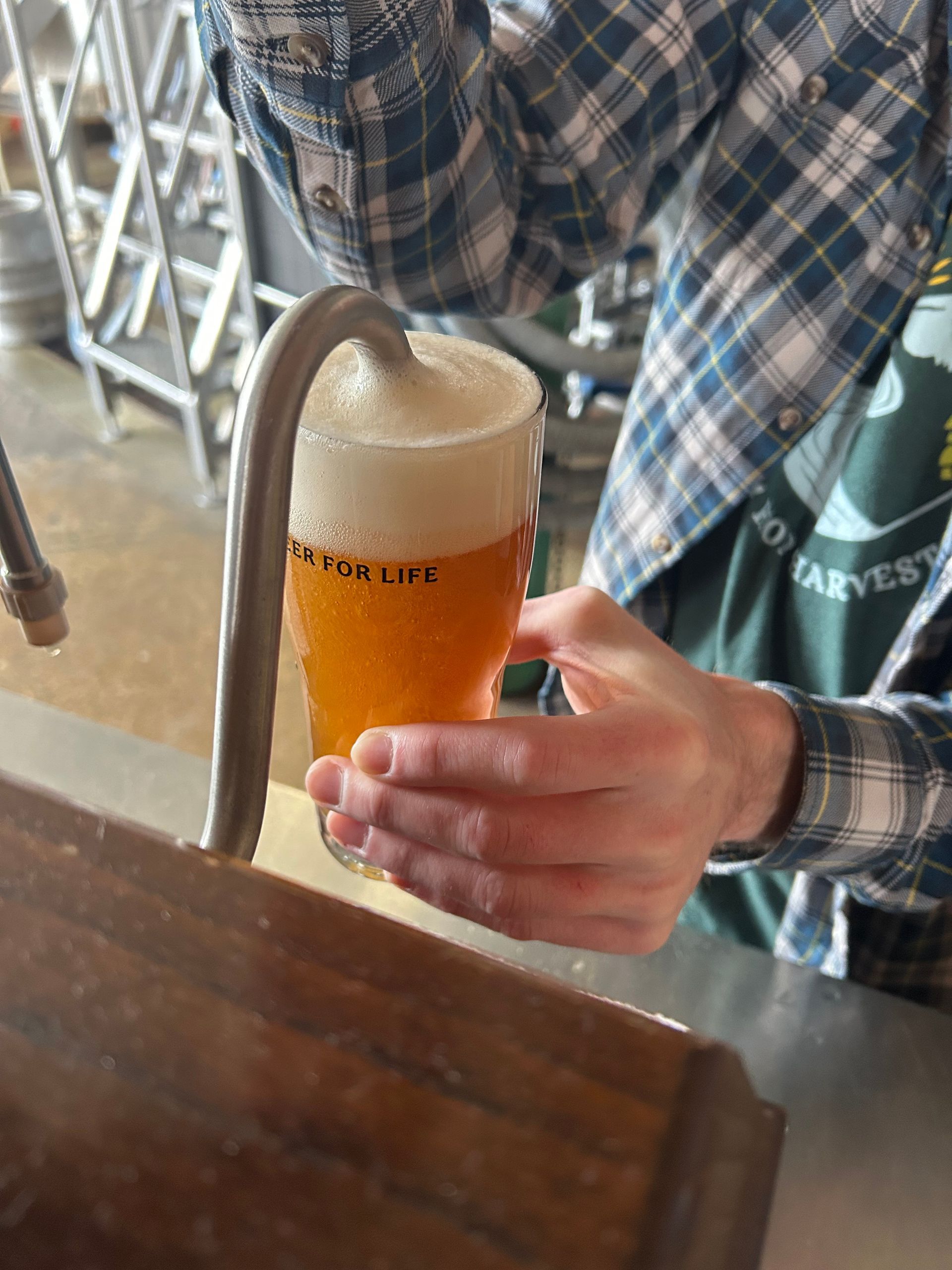 Person pouring beer from tap into a glass, creating a foamy head; indoors.