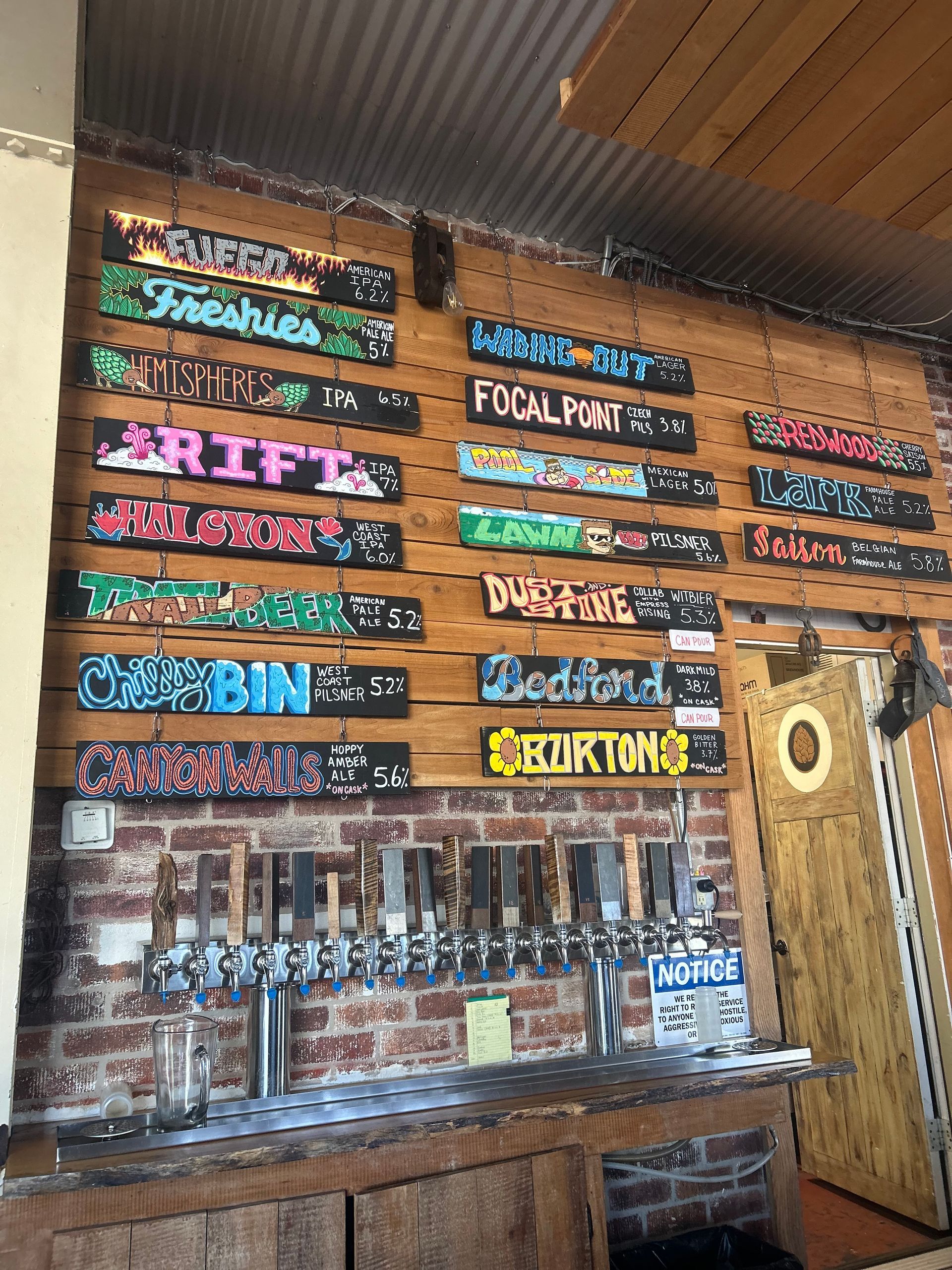 Taproom with wooden signs listing beer options above taps on a brick and wood wall.