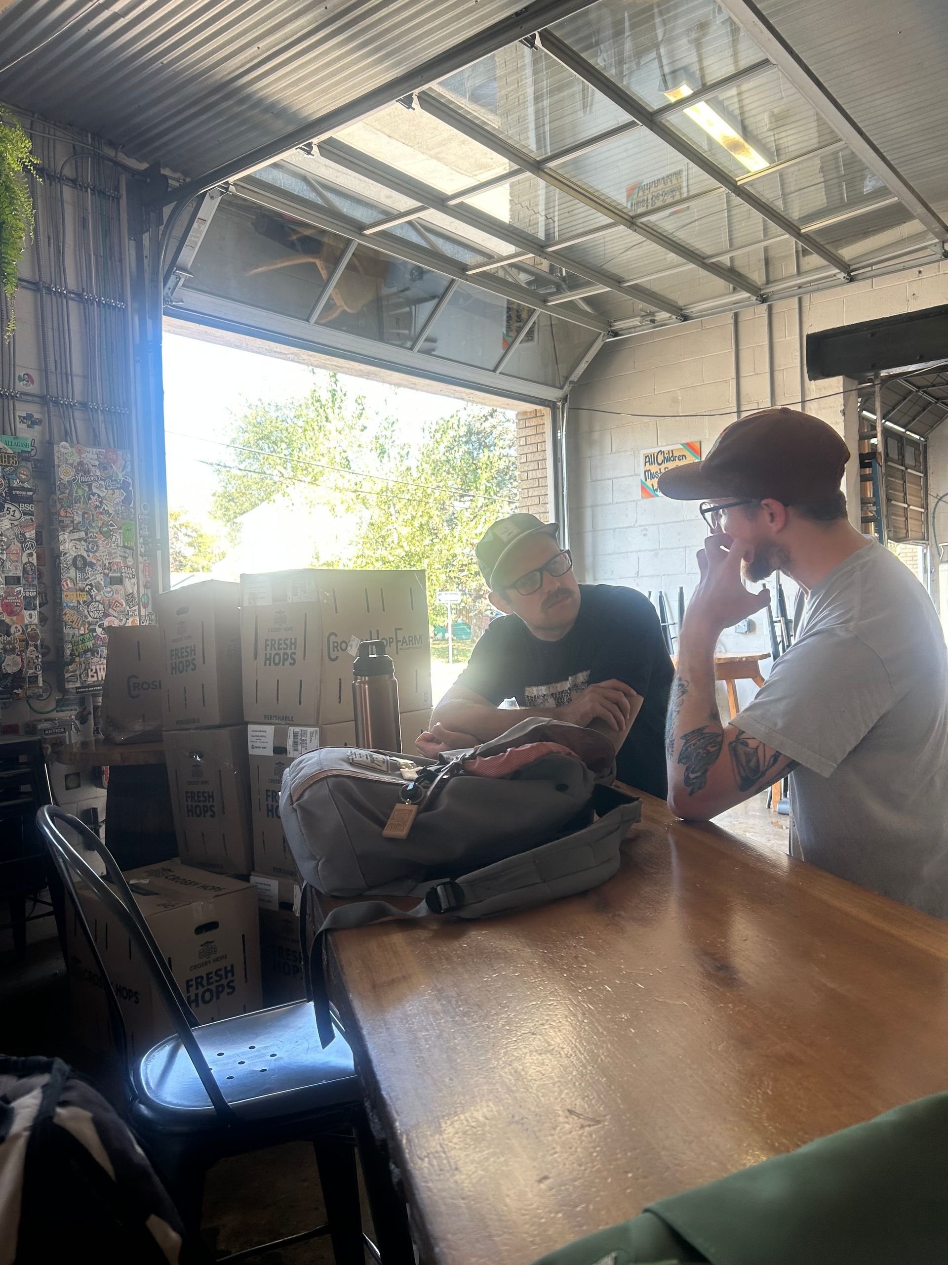 Two people at a bar in a warehouse, looking at a bag, with sunlight streaming in.