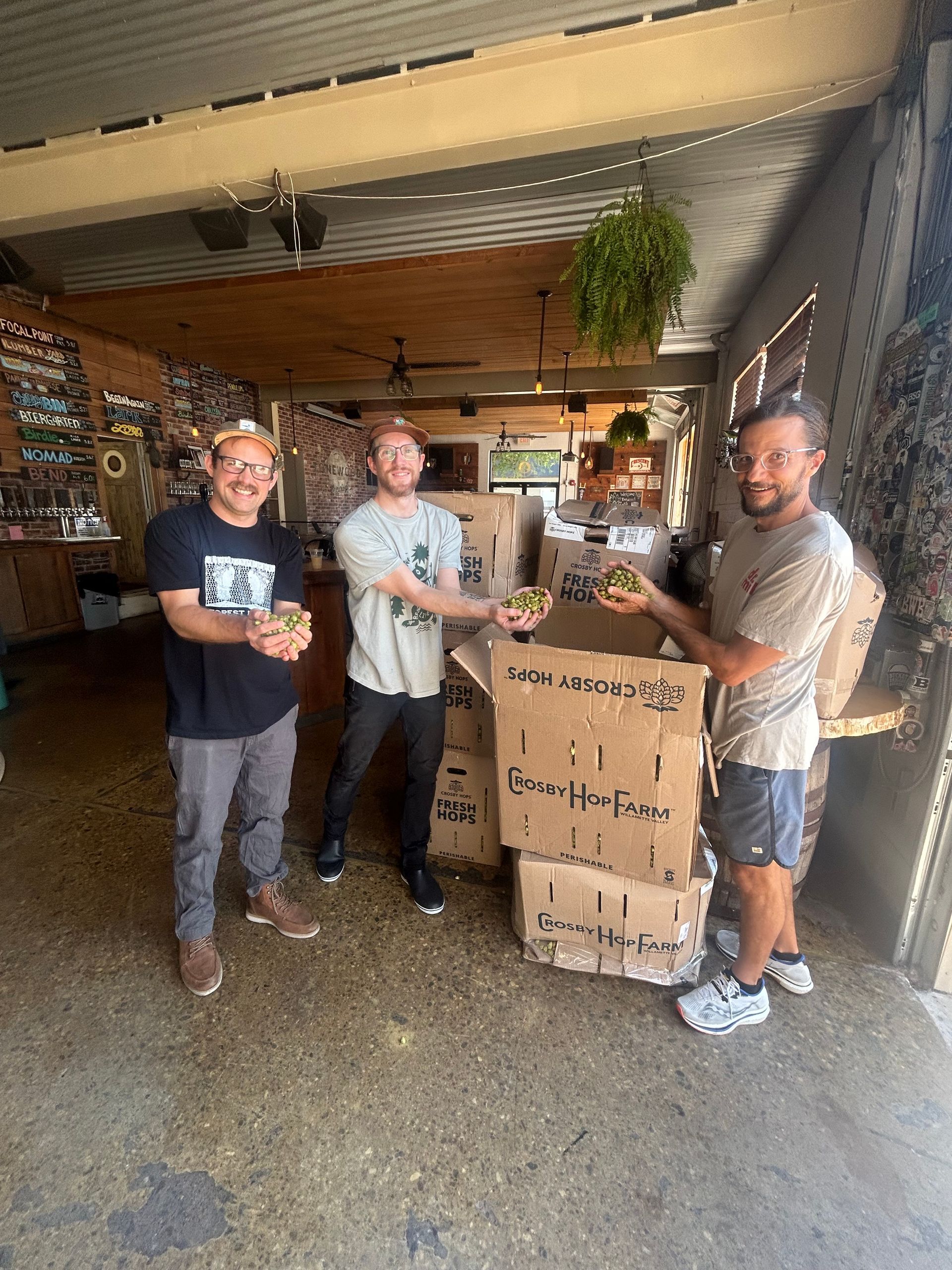 Three people holding food items near boxes in an open-air building.