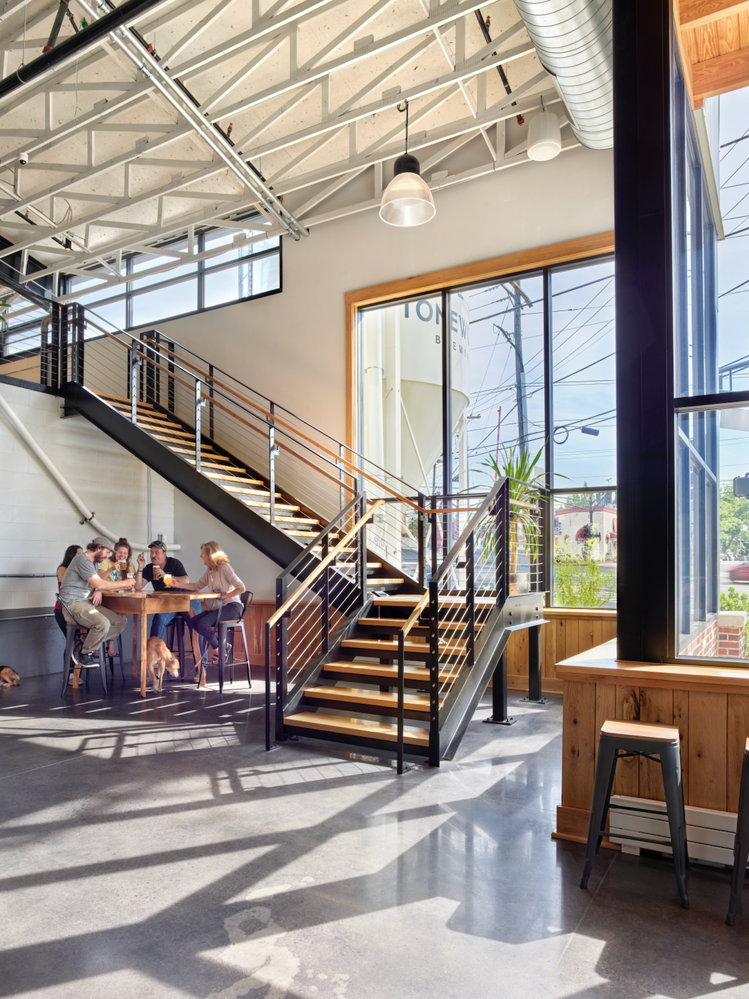 Interior with industrial staircase, people at table, and large windows with natural light.