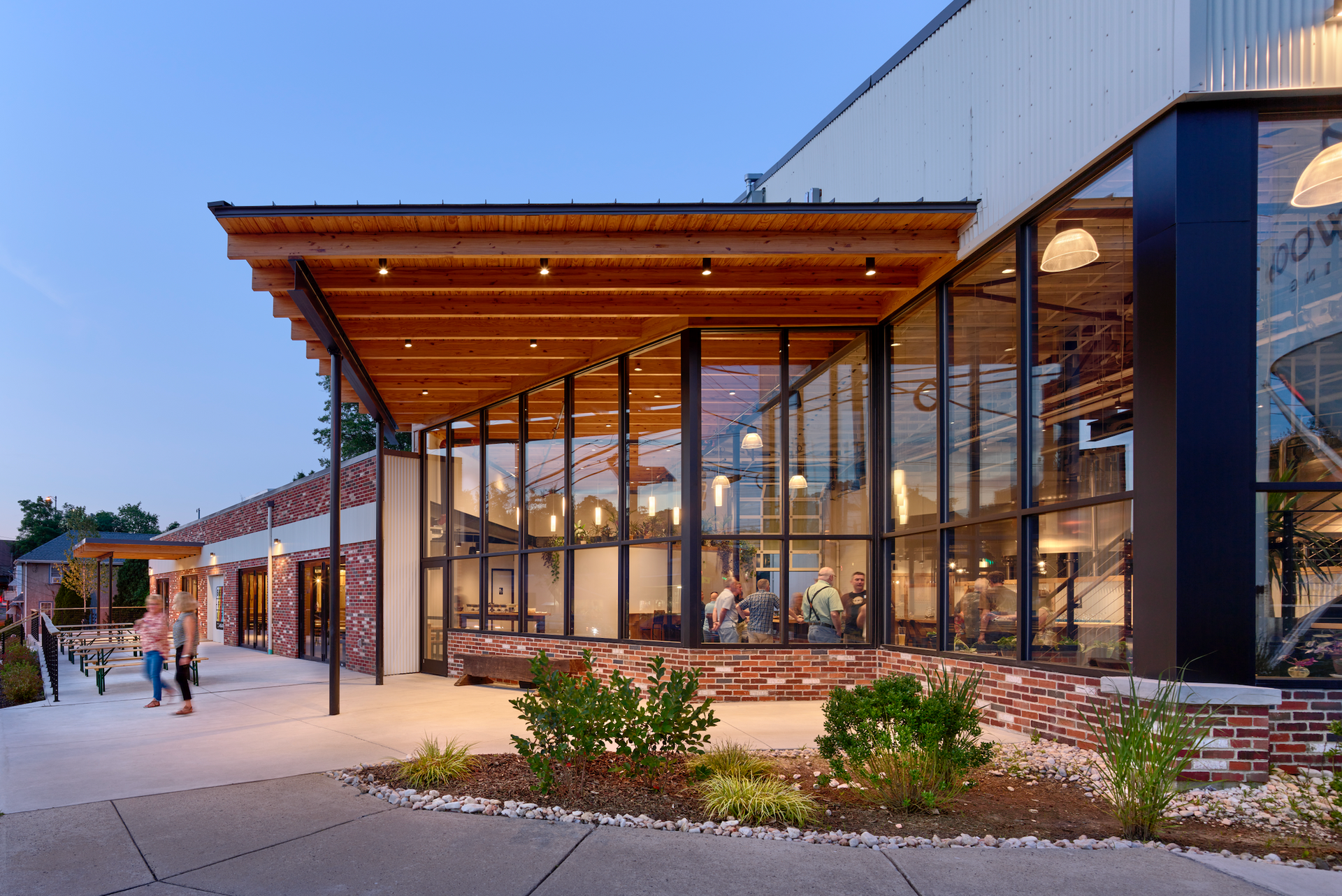 Modern building entrance with large glass windows and wooden overhang; people walk past.