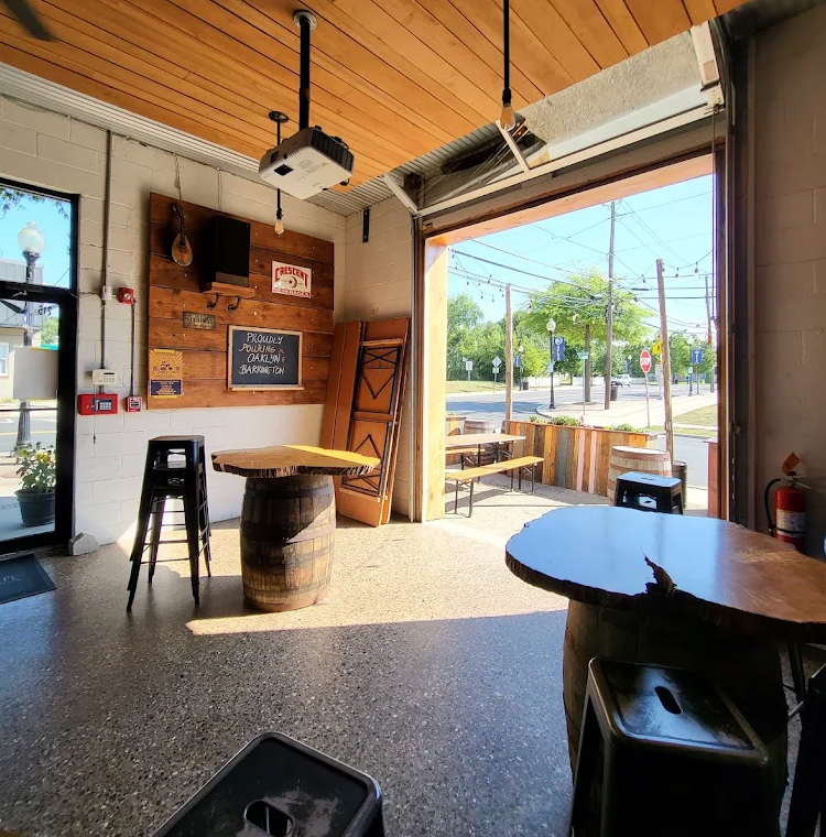 Interior of a bar with a barrel table, open doorway to street. Wooden paneling, concrete floor, overhead projector.