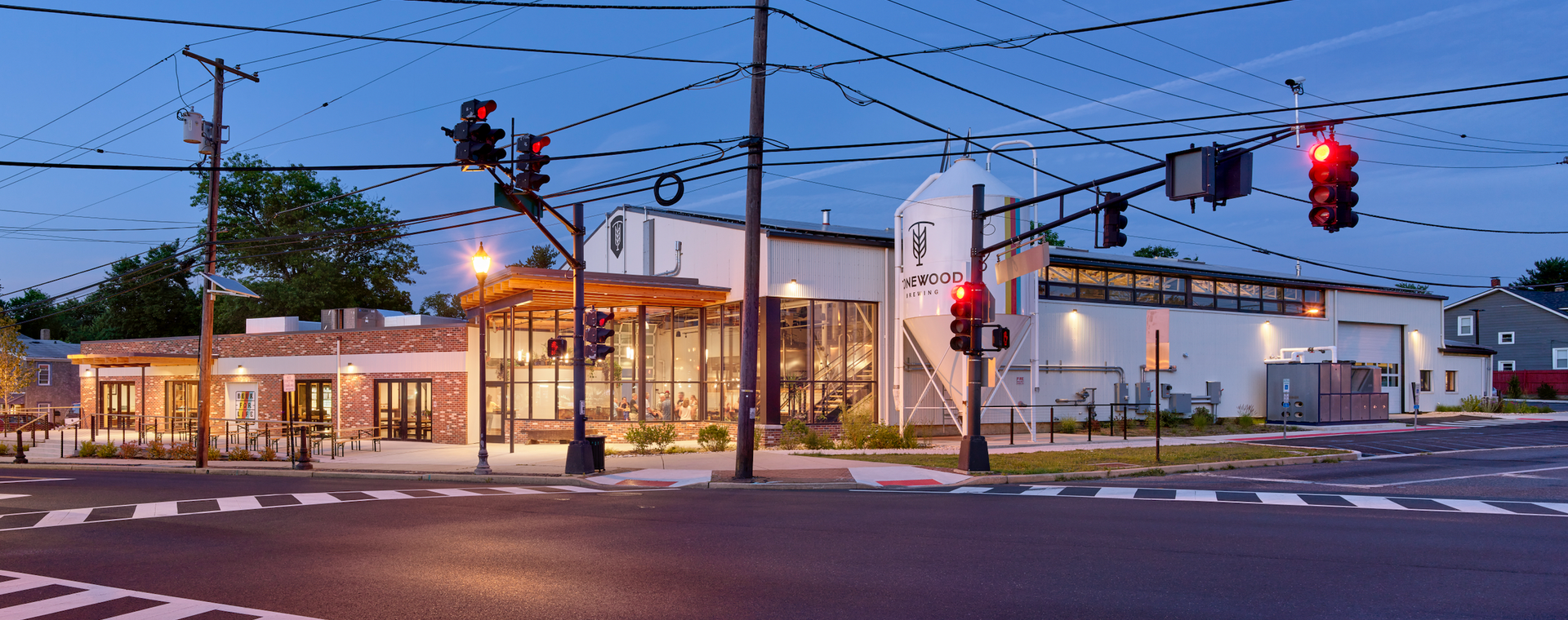 Building at an intersection at dusk with traffic lights and power lines.
