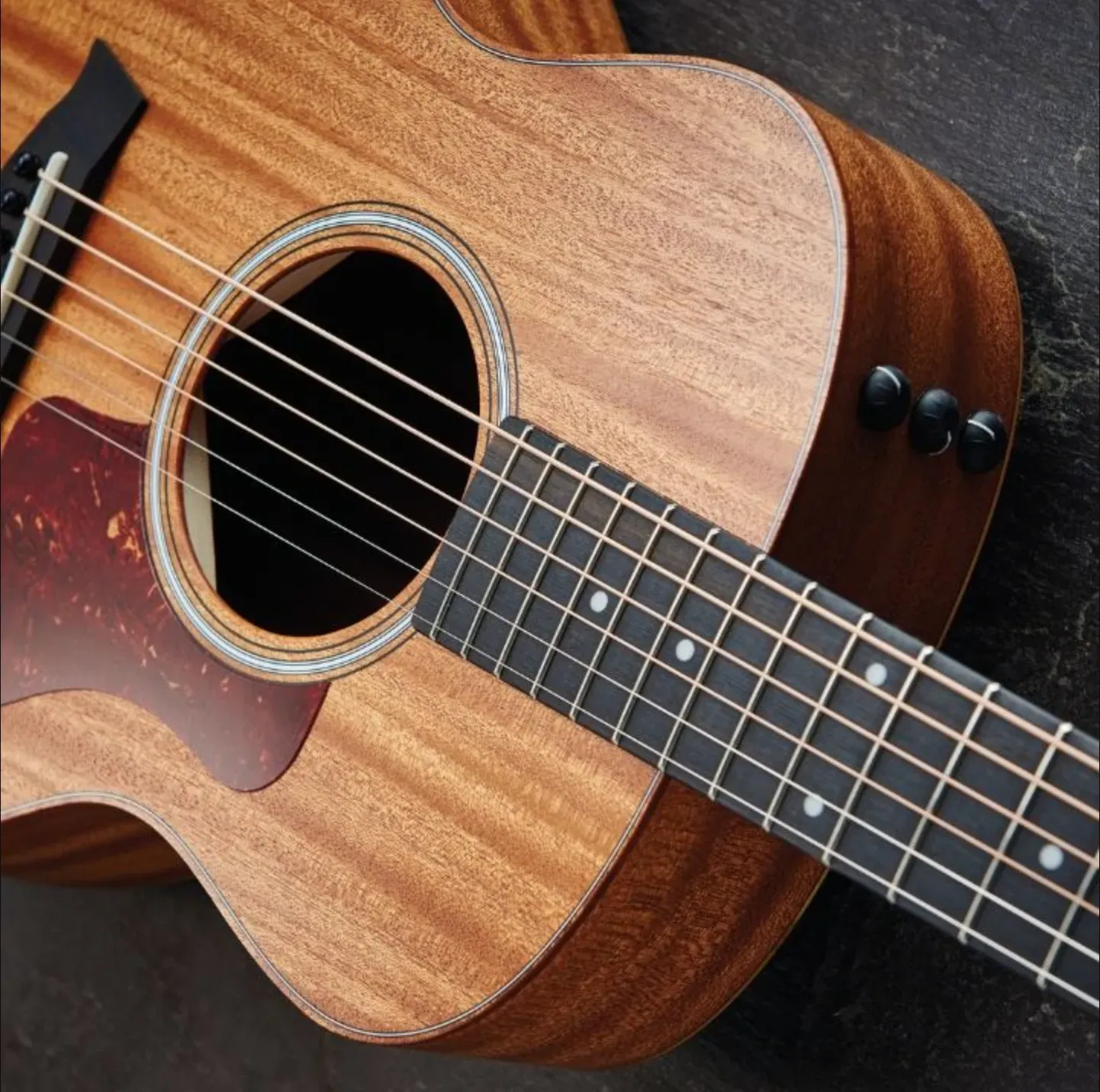 Close-up of a brown acoustic guitar; neck angled toward the viewer; strings visible.