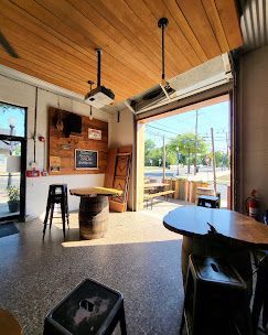 Interior of a bar with open doors. Wooden ceiling, barrel tables, stools, and concrete floor.