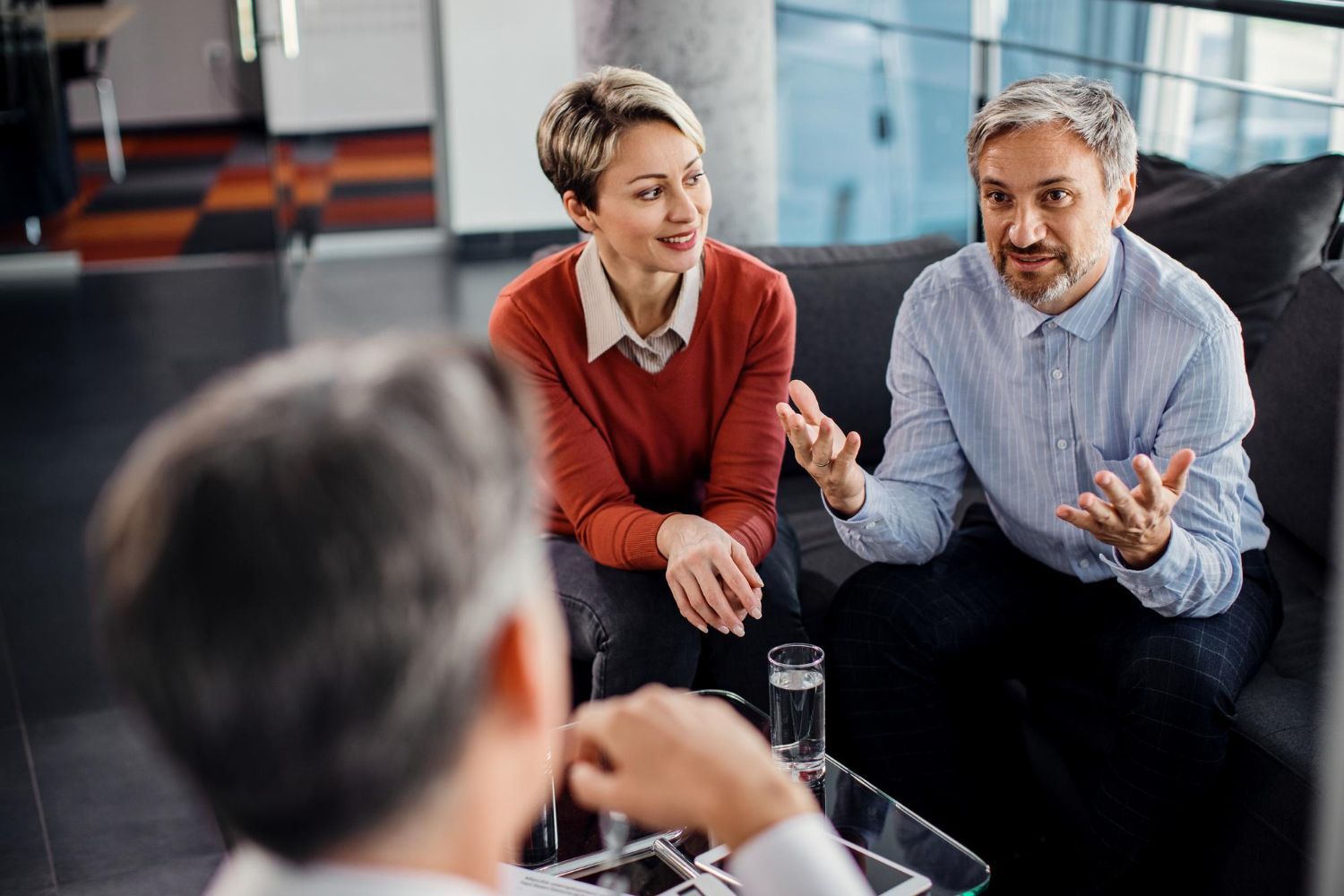A man and a woman are sitting on a couch talking to a man.
