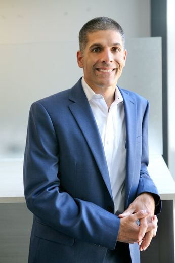 A man in a blue suit and white shirt is standing in front of a window.