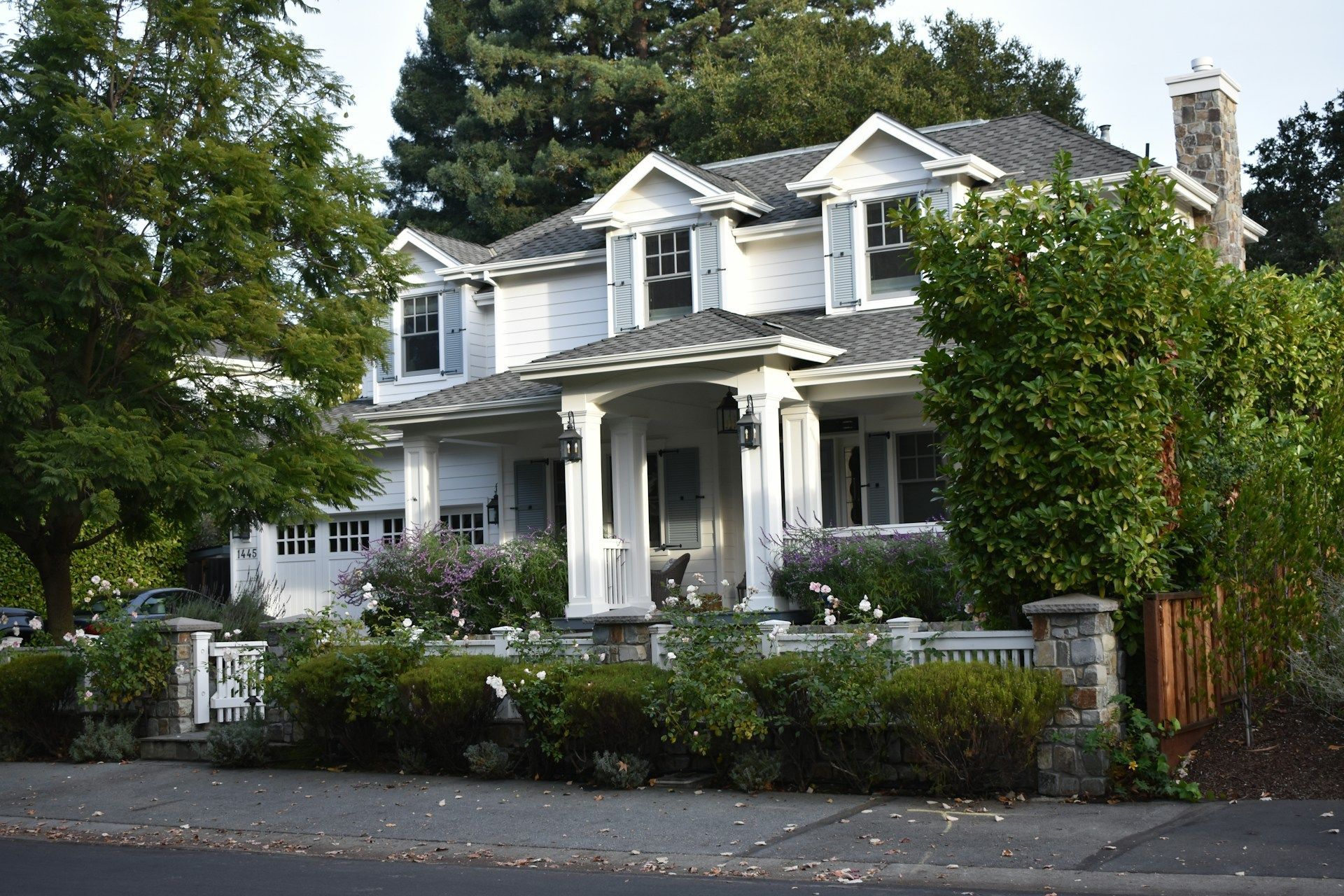 A large white house with a gray roof is surrounded by trees