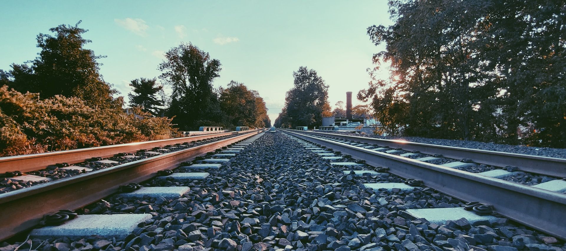 A train track with trees in the background and the sun shining through the trees.
