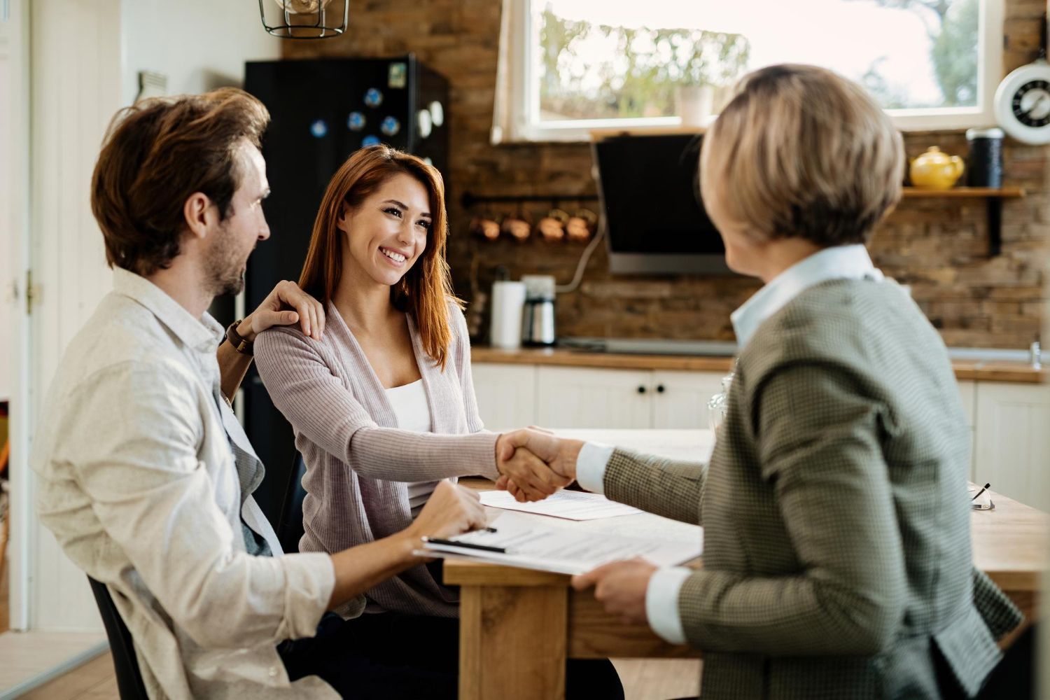 Couple shakes hands with a professional at a wooden table, kitchen setting.