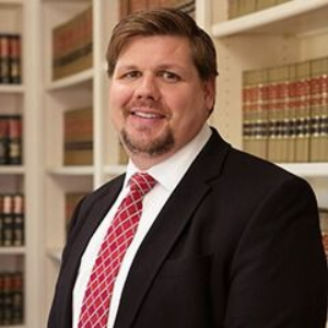 Man in suit and tie, smiling in a library setting, bookshelves in the background.