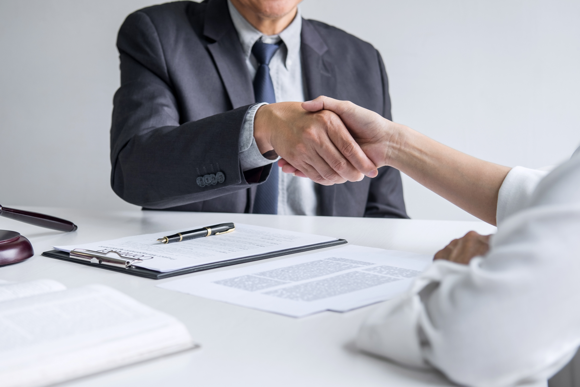 A man in a suit shaking hands with a person at a desk with documents.