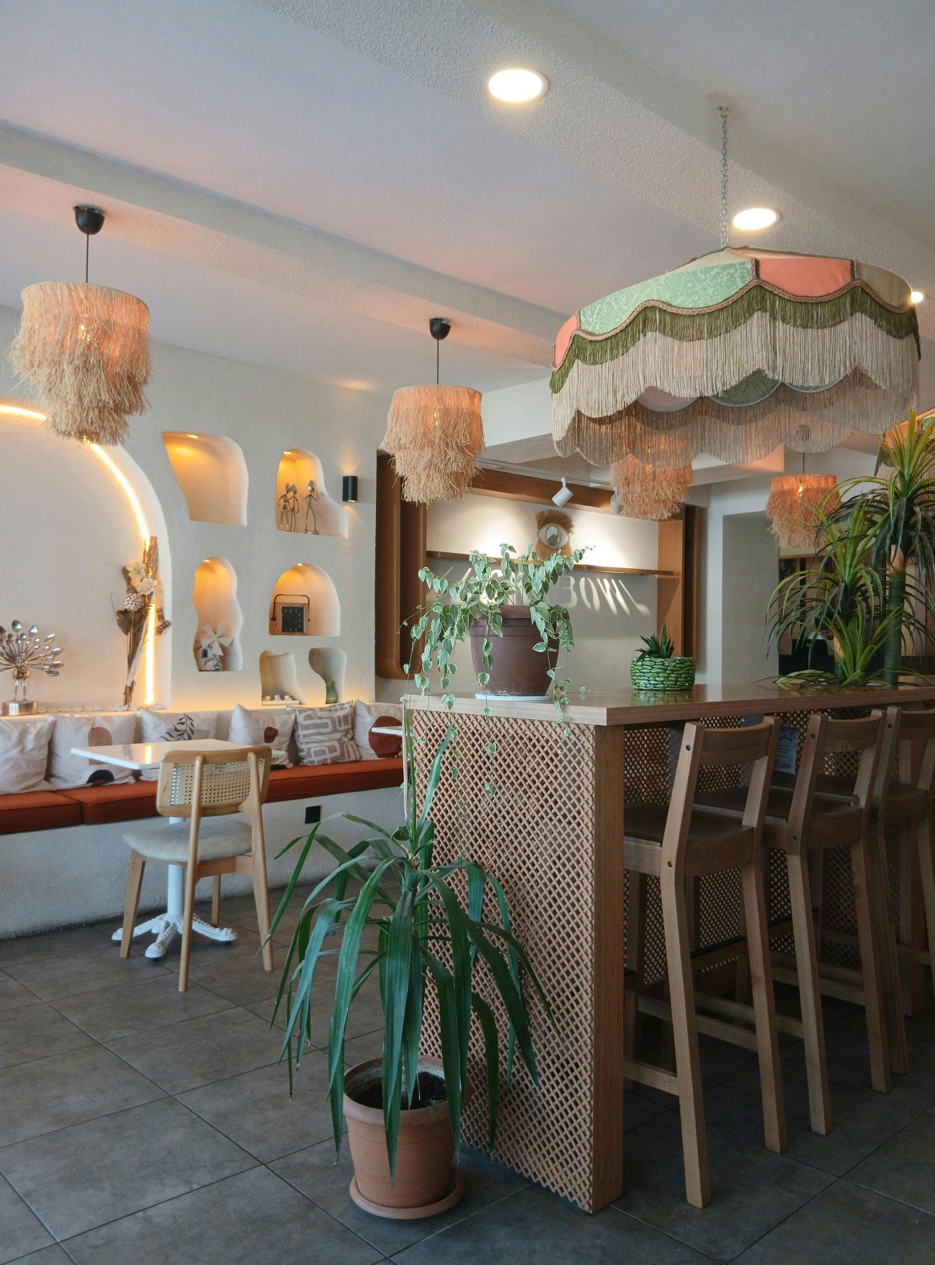 Interior of a cafe with rattan accents, fringed lamps, and a bar with wooden stools.