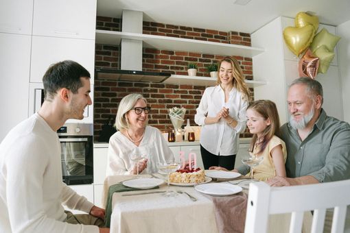 Family celebrating a birthday; a cake with candles on the table, balloons, and happy expressions in a kitchen.