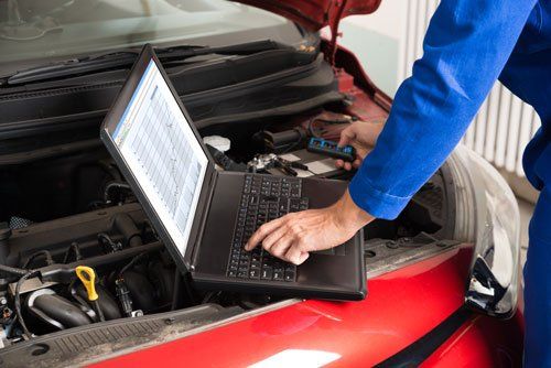 un computer portatile appoggiato sul motore d una macchina con il cofano aperto e il raccio di un meccanico mentre lo utilizza