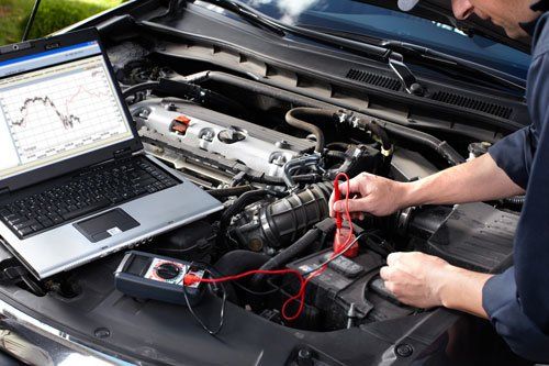 un meccanico utilizza un tester collegato a un computer portatile appoggiato sul motore di una macchina