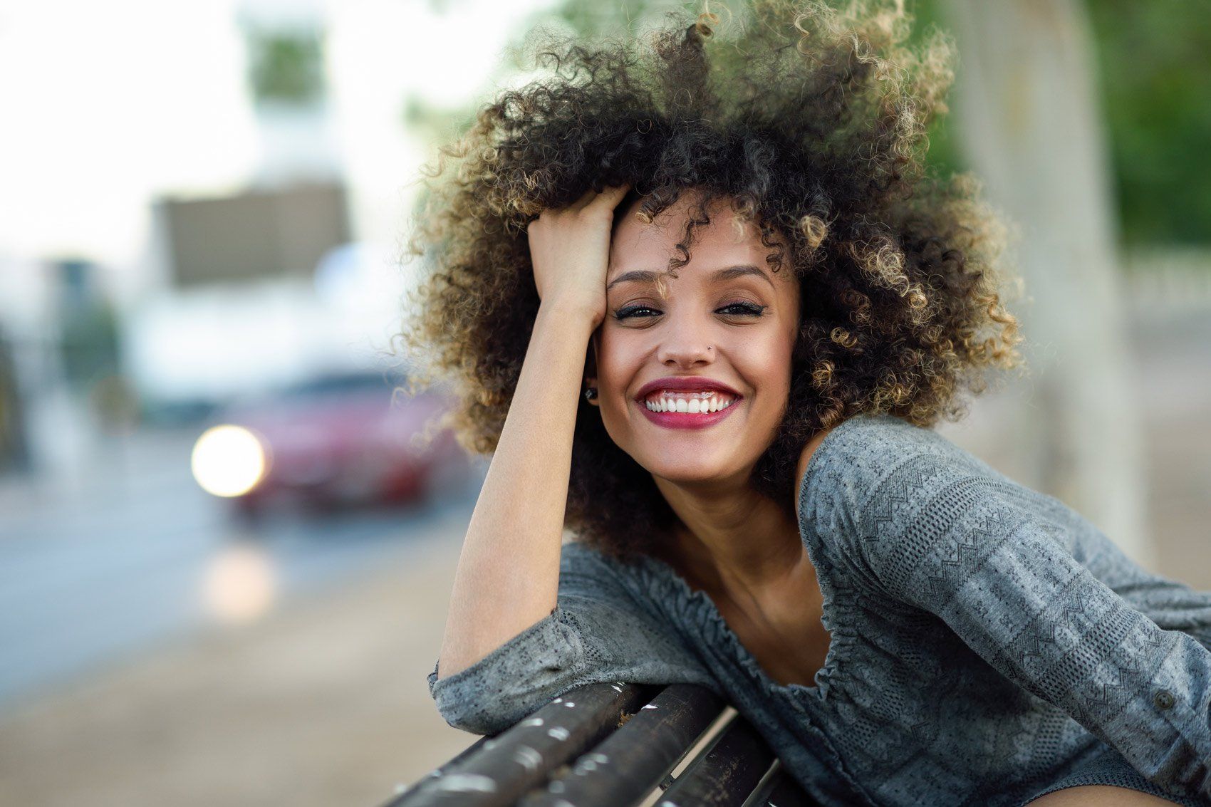 A woman with curly hair is sitting on a bench and smiling.