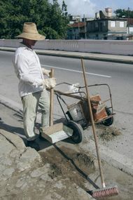 A man wearing a straw hat is sweeping the sidewalk