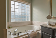 A bathroom with a jacuzzi tub , sink , mirror and window.