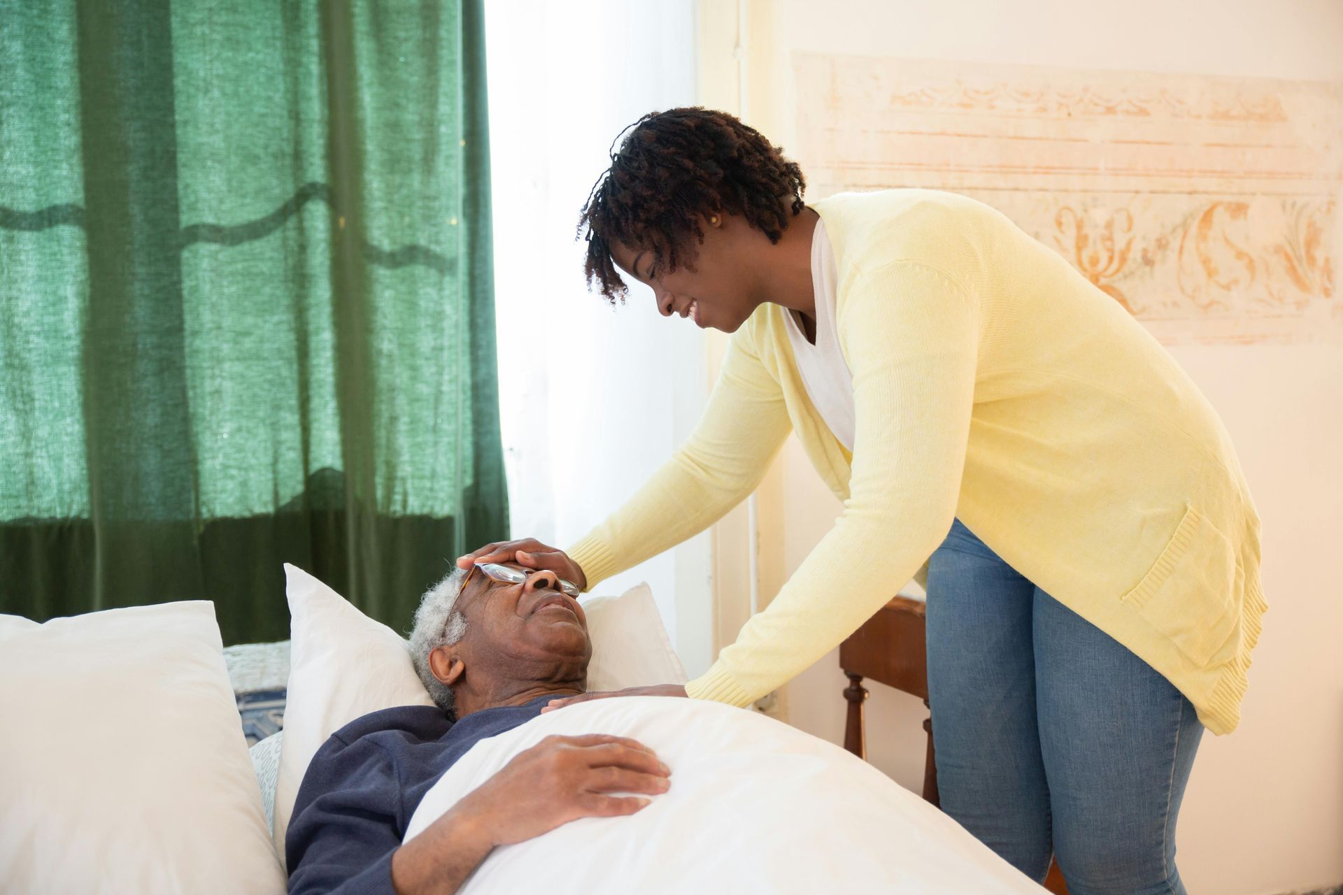 A woman is taking the temperature of an elderly man in a bed.