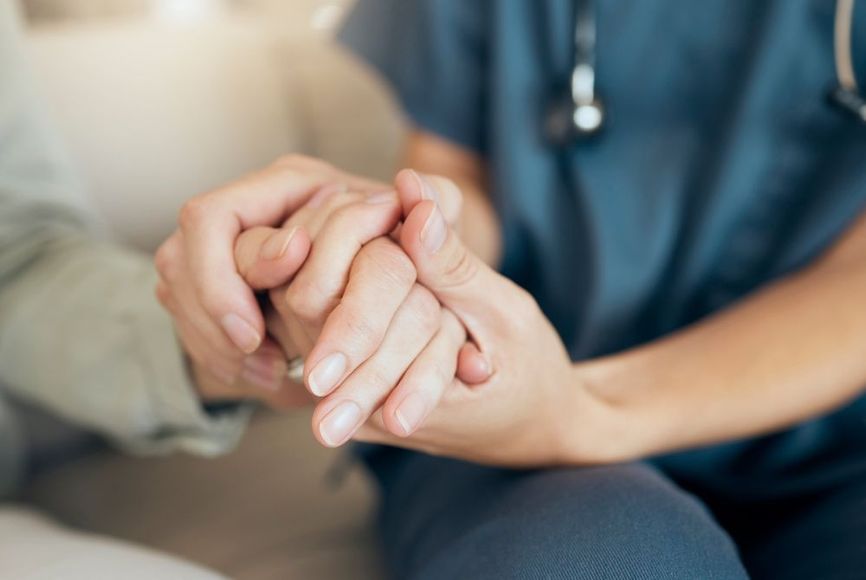 A nurse is holding the hand of an elderly woman.