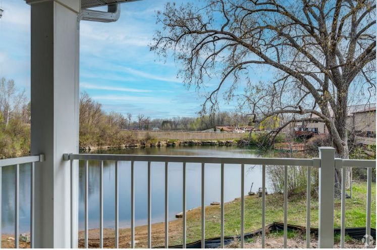 Porch railing overlooking a calm lake with bare trees and blue sky