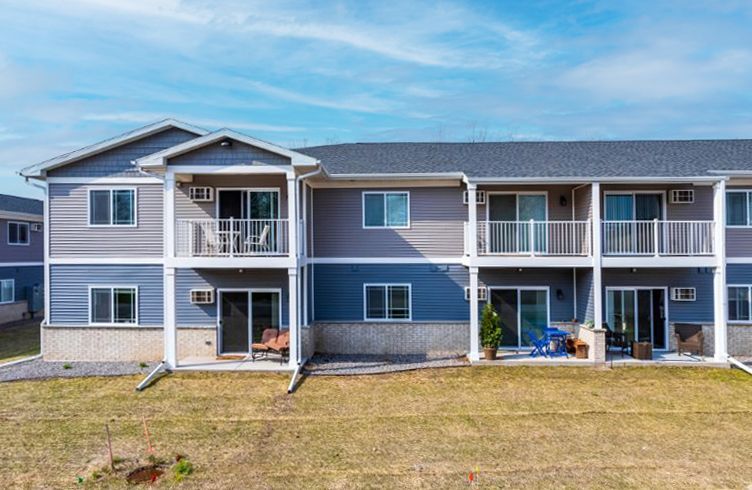 Two-story blue apartment building with white trim, balconies, and a grassy front lawn