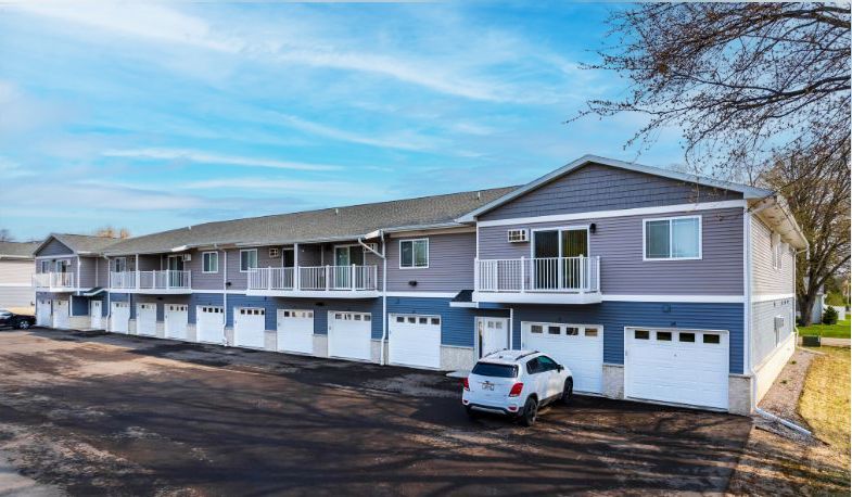 Two-story apartment building with garages and a white SUV parked outside under a blue sky