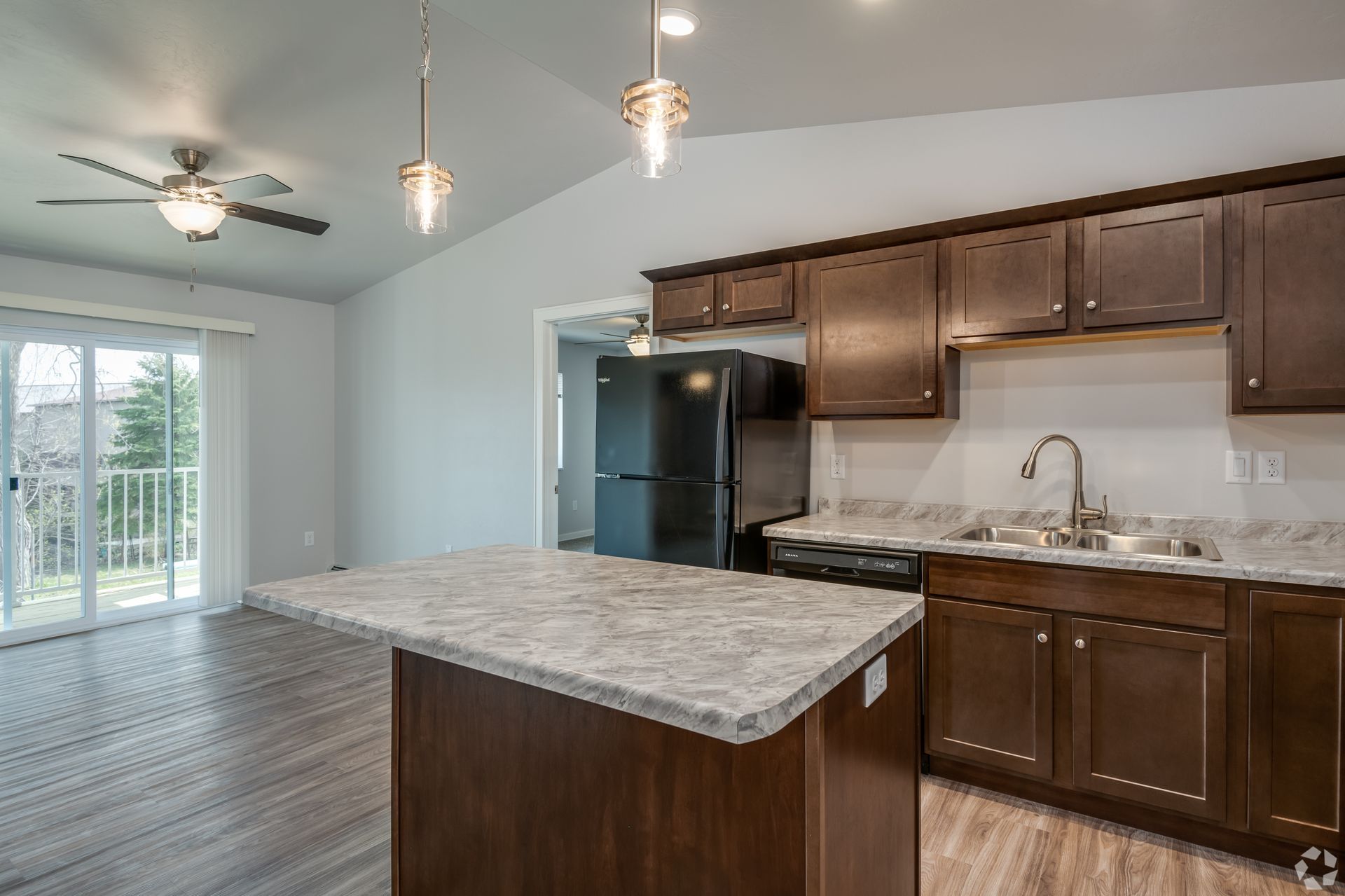 Modern kitchen with dark wood cabinets, granite island, stainless sink, black fridge, and sliding glass doors to patio
