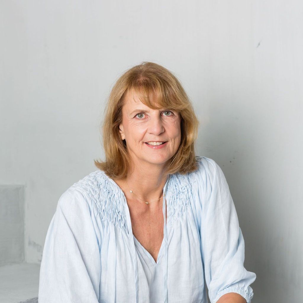 A woman in a light blue shirt is sitting in a chair and smiling.