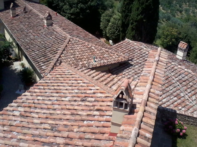 Tetto in tegole di argilla di un edificio, visto dall'alto, con diversi camini.