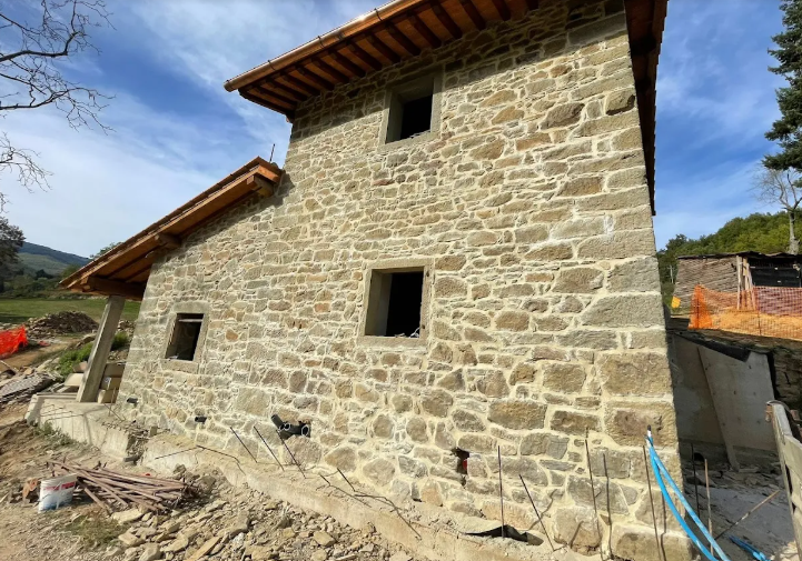 Edificio in pietra con travi a vista, in costruzione contro un cielo parzialmente nuvoloso.