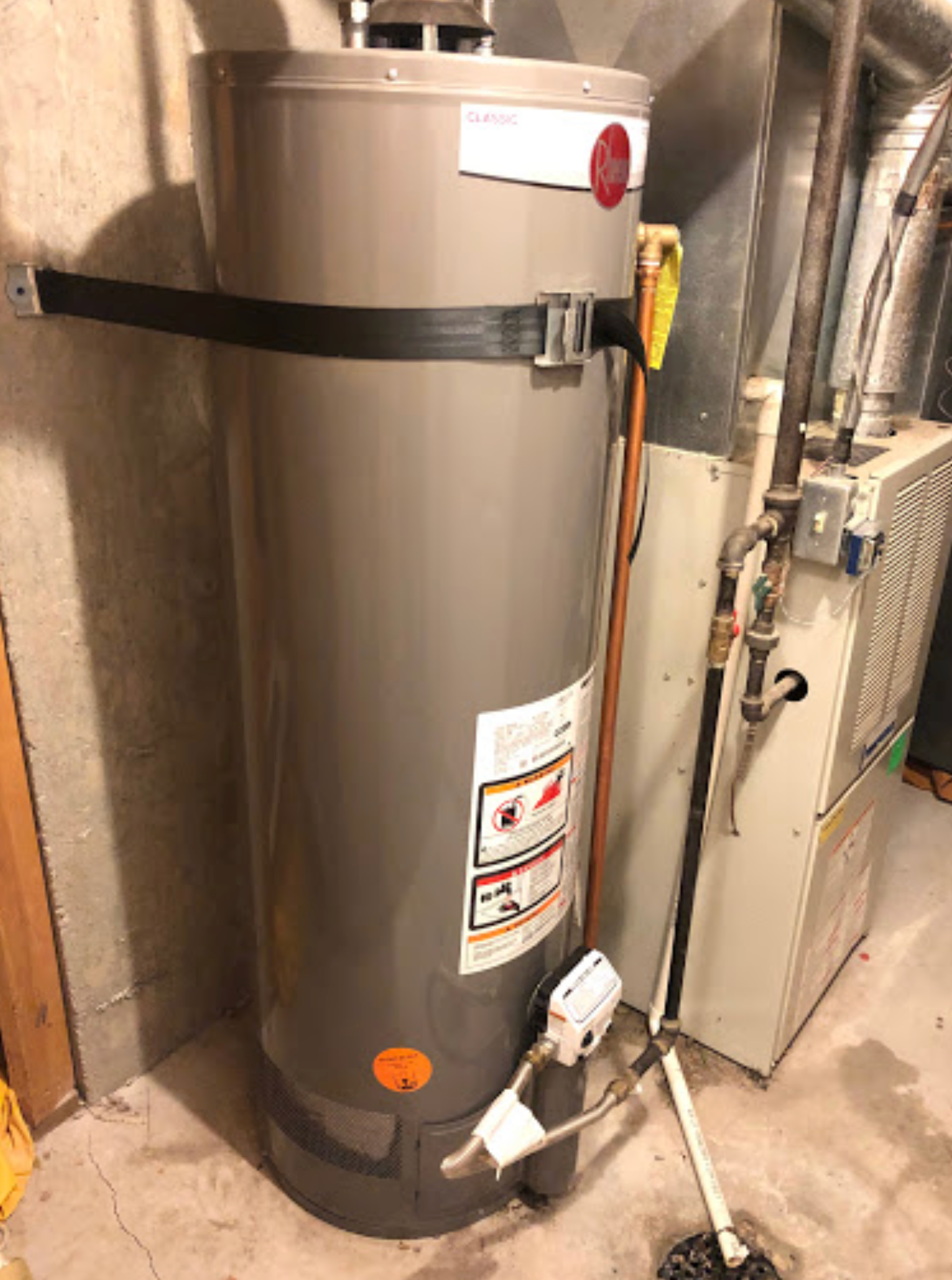 A water heater is sitting in a basement next to a furnace.