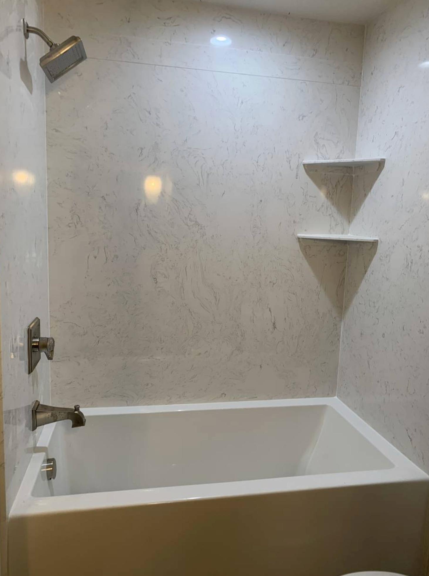 A bathroom with a bathtub , shower , toilet and shelves.