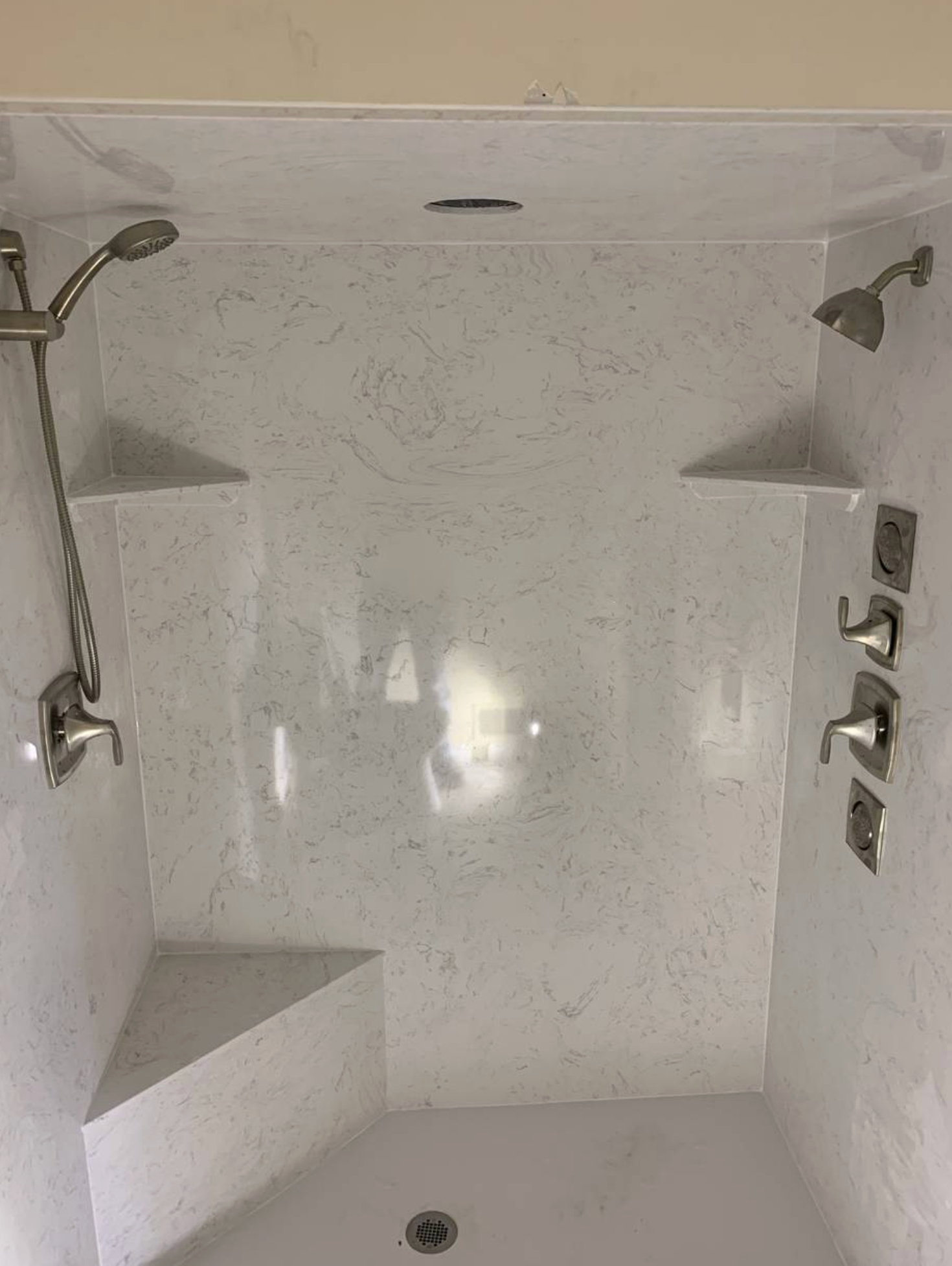 A shower with two shower heads and shelves in a bathroom.