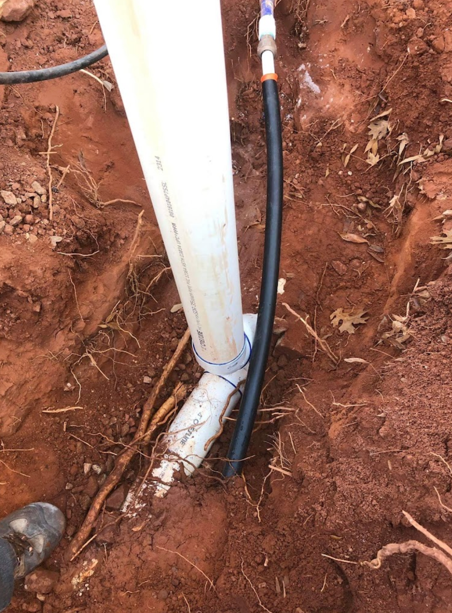 A white pipe is sitting in the dirt next to a black pipe.