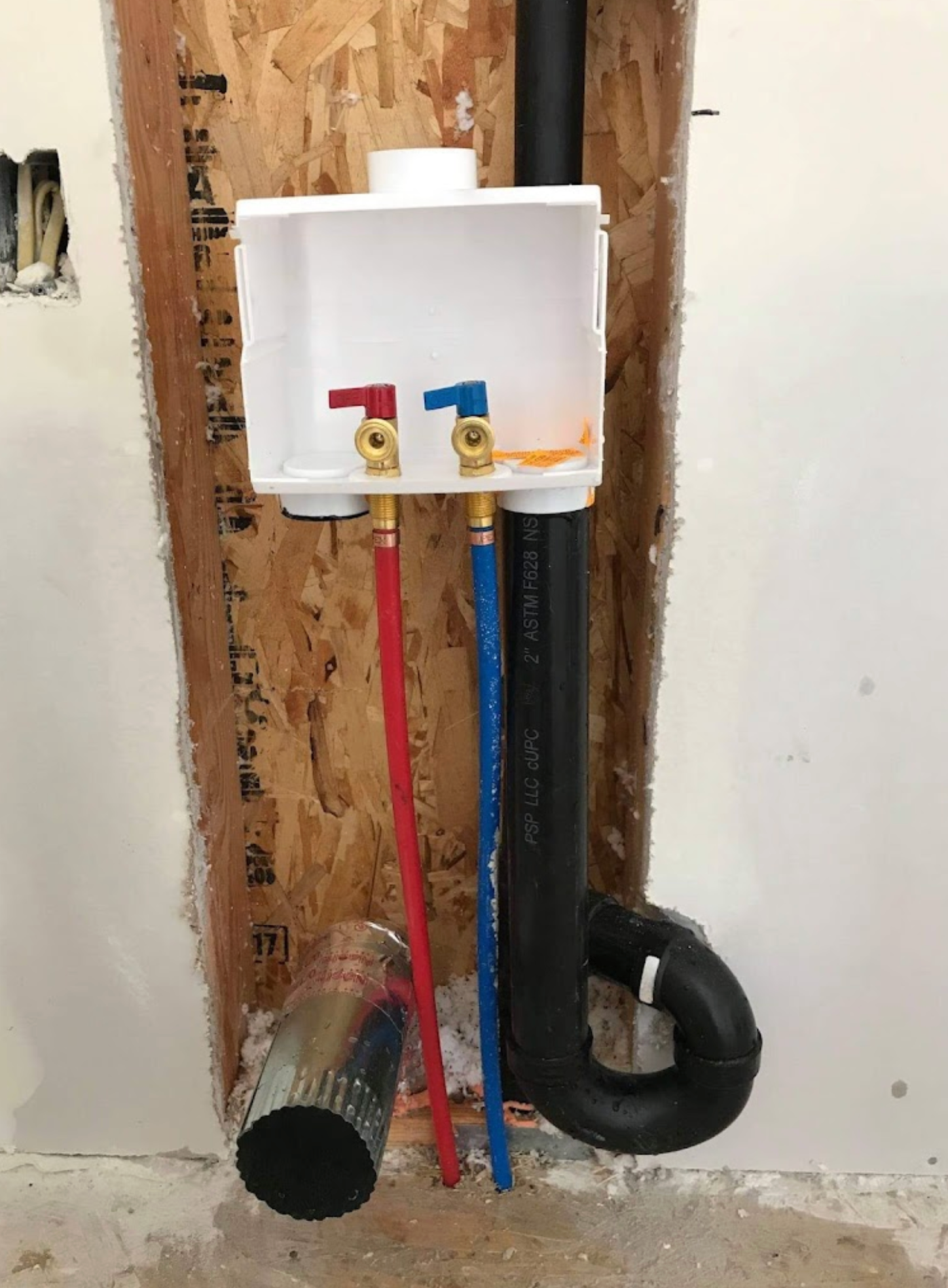 A washer and dryer drain box is being installed in a wall.