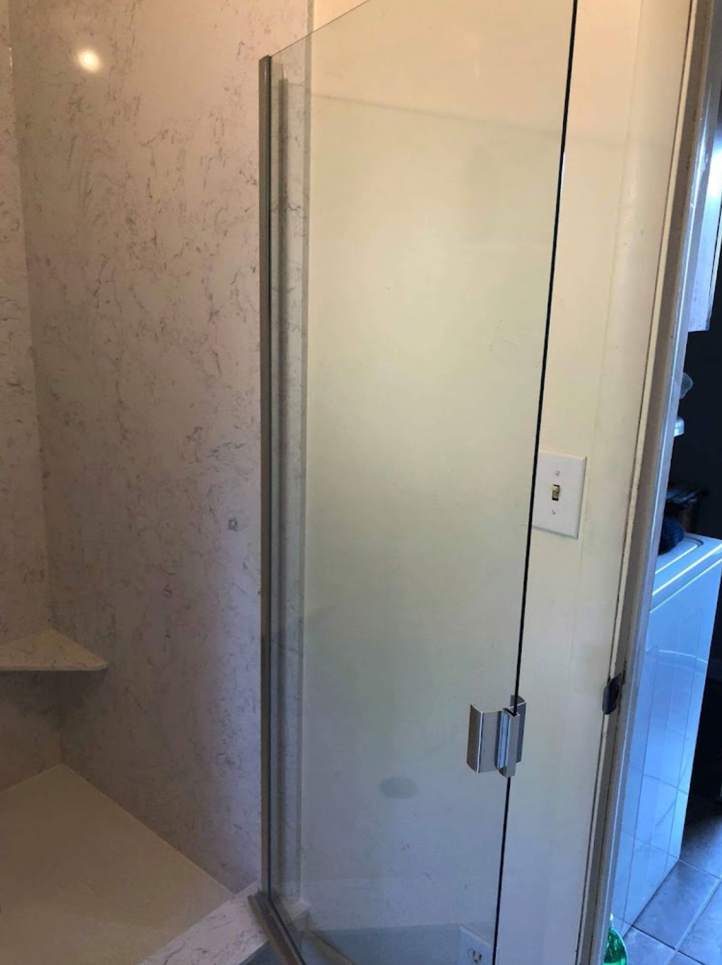 A bathroom with a glass shower door and a marble wall.