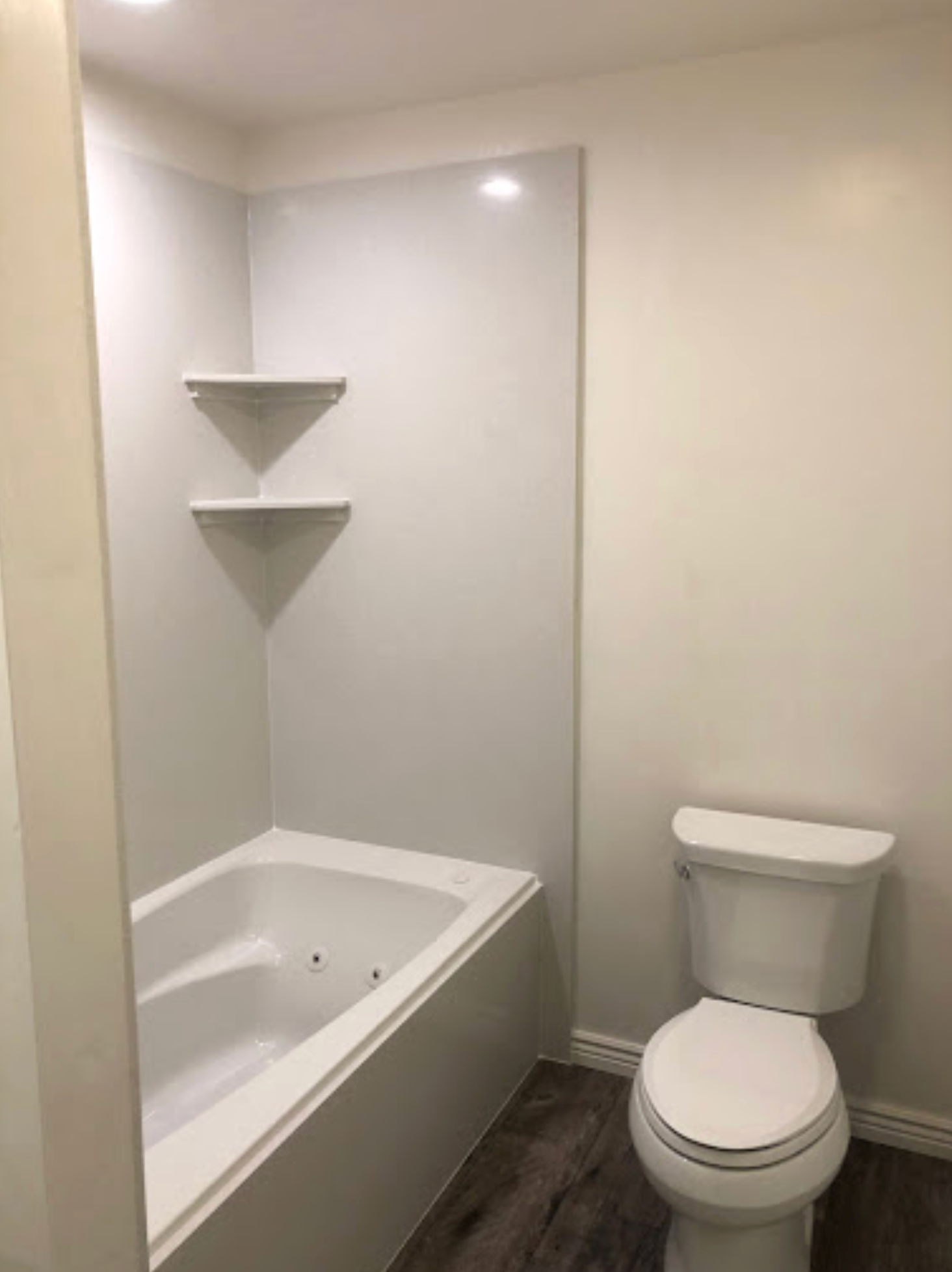 A bathroom with a tub , toilet and shelves.