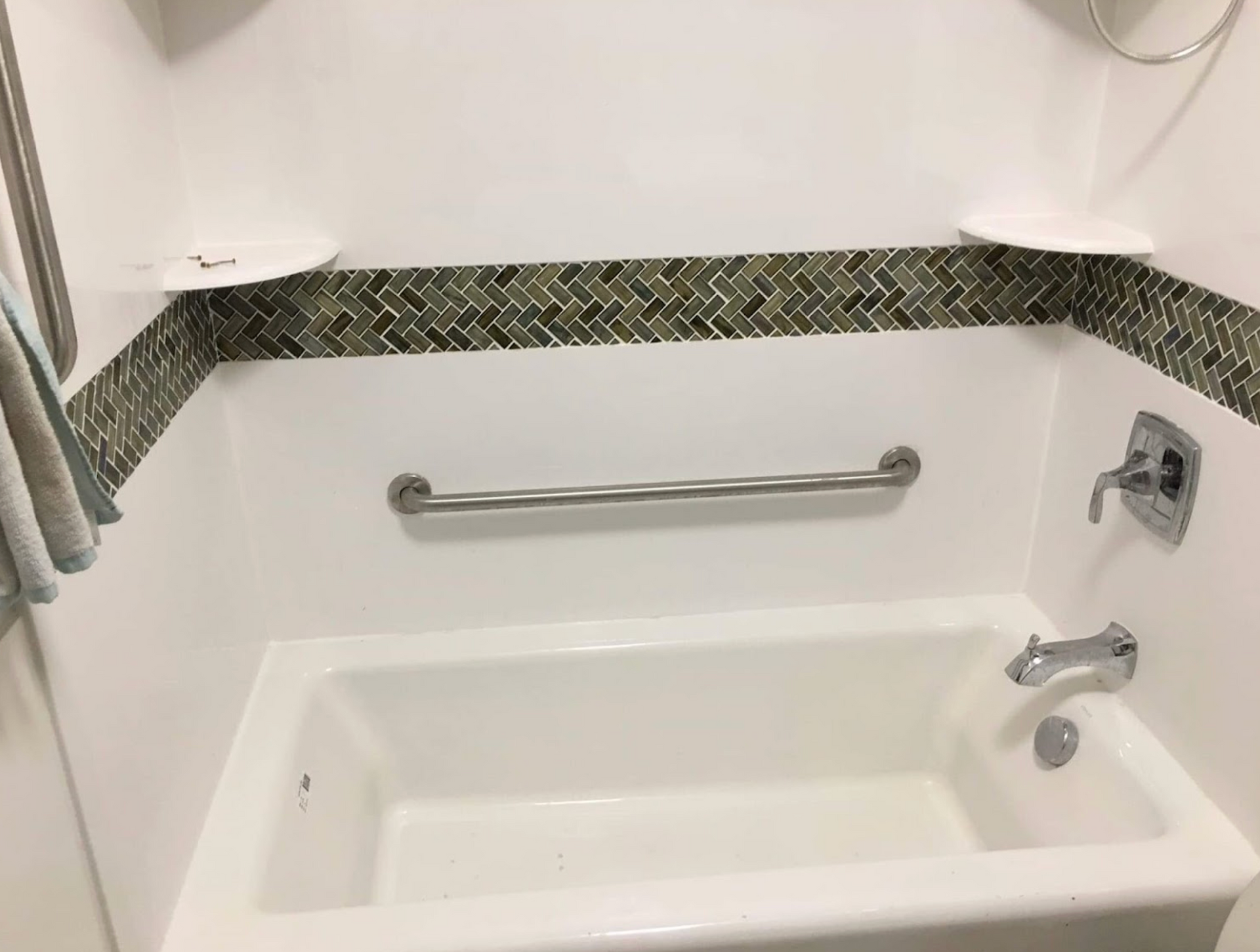 A white bathtub with a stainless steel railing in a bathroom.