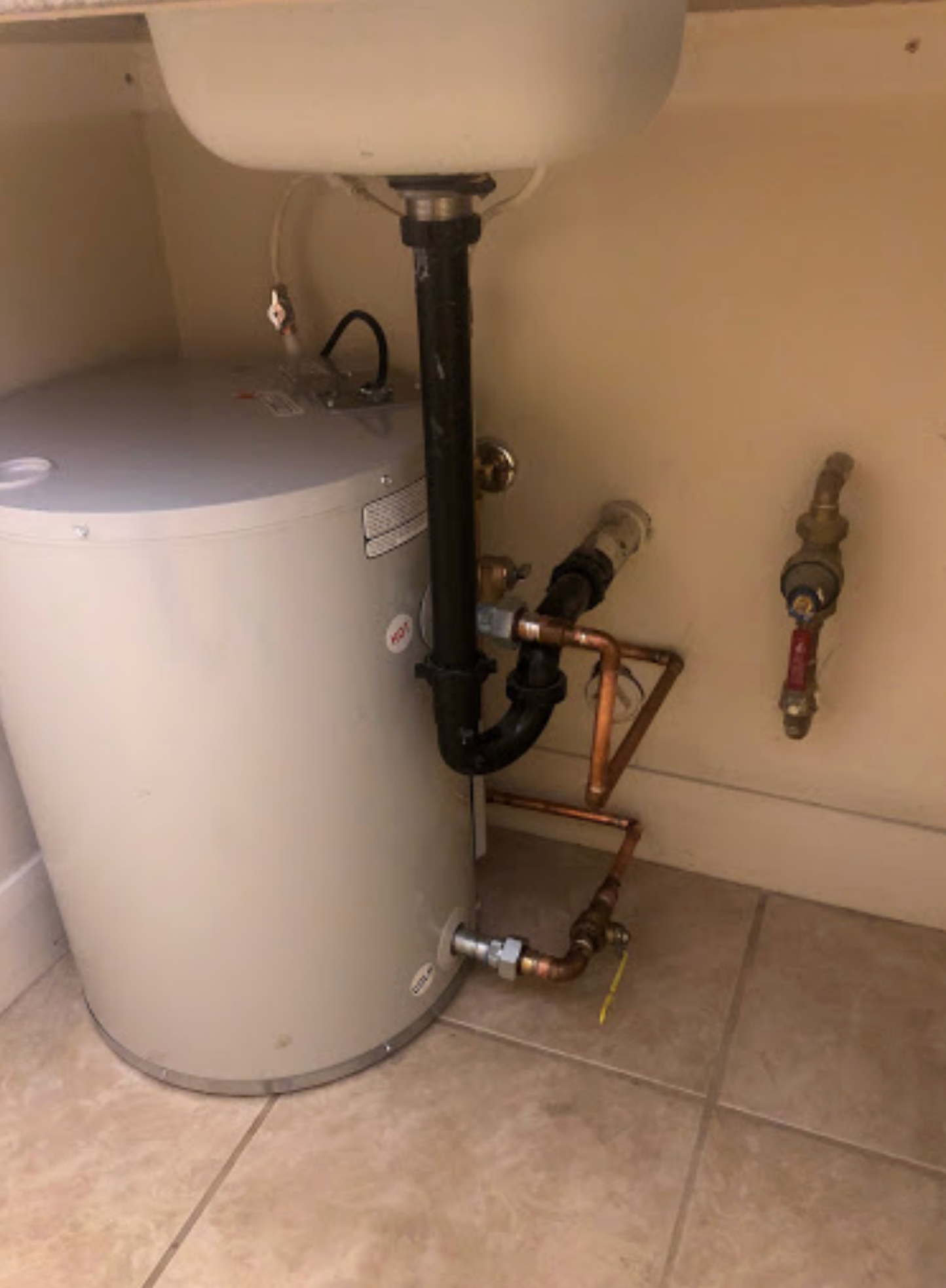 A water heater is under a sink in a bathroom.