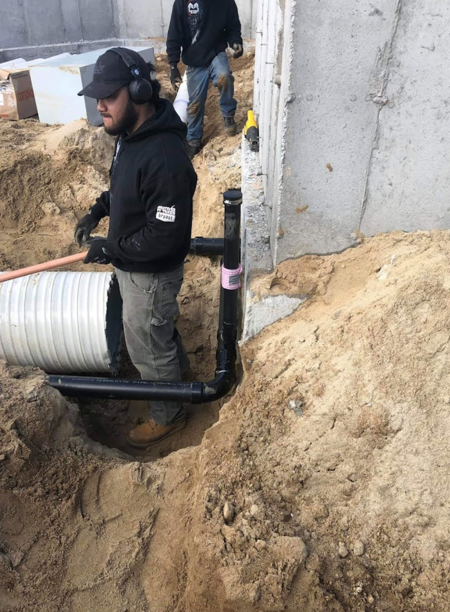 A man is standing in the dirt next to a pipe.
