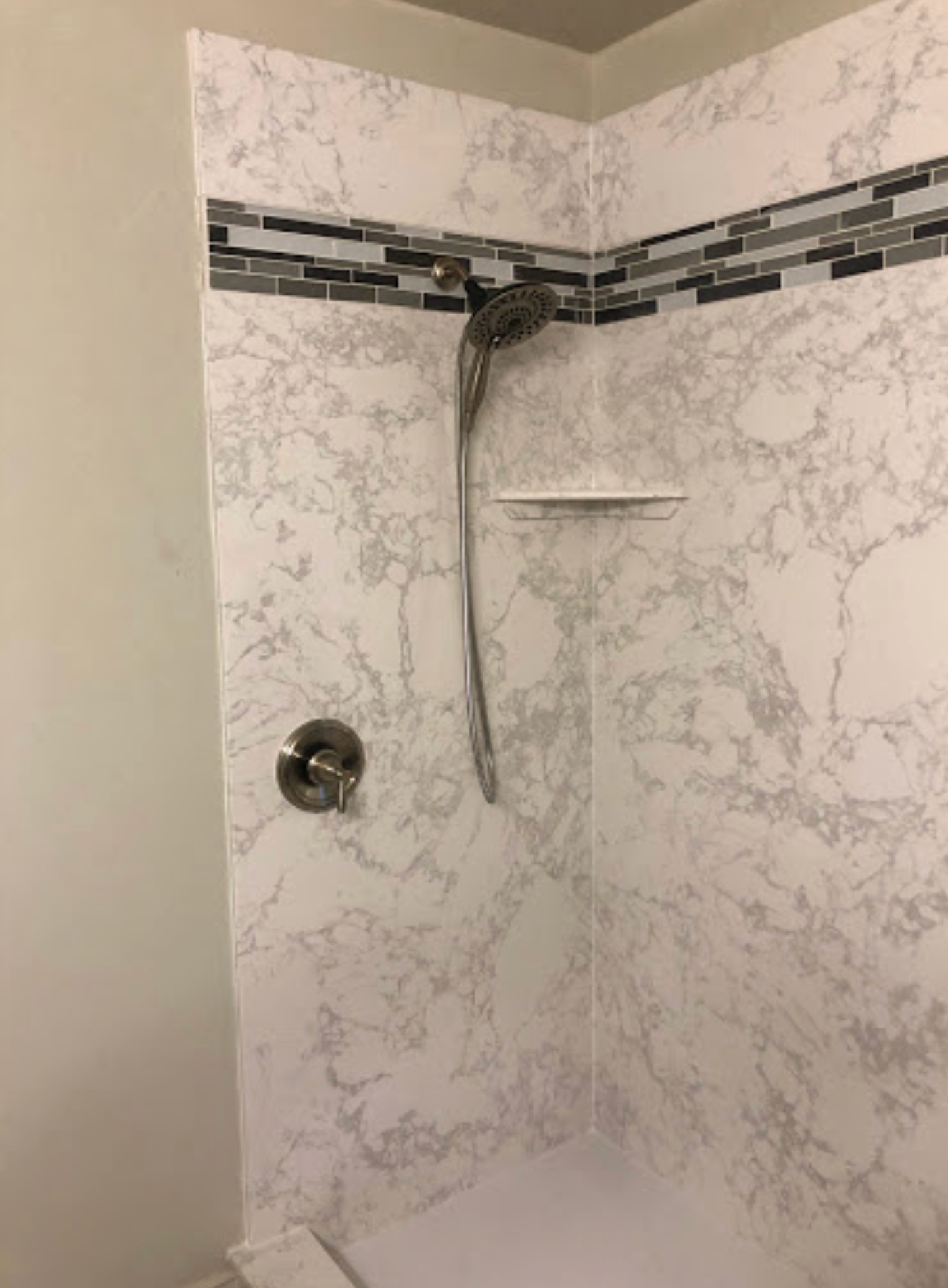 A shower with a shower head and a shelf in a bathroom.