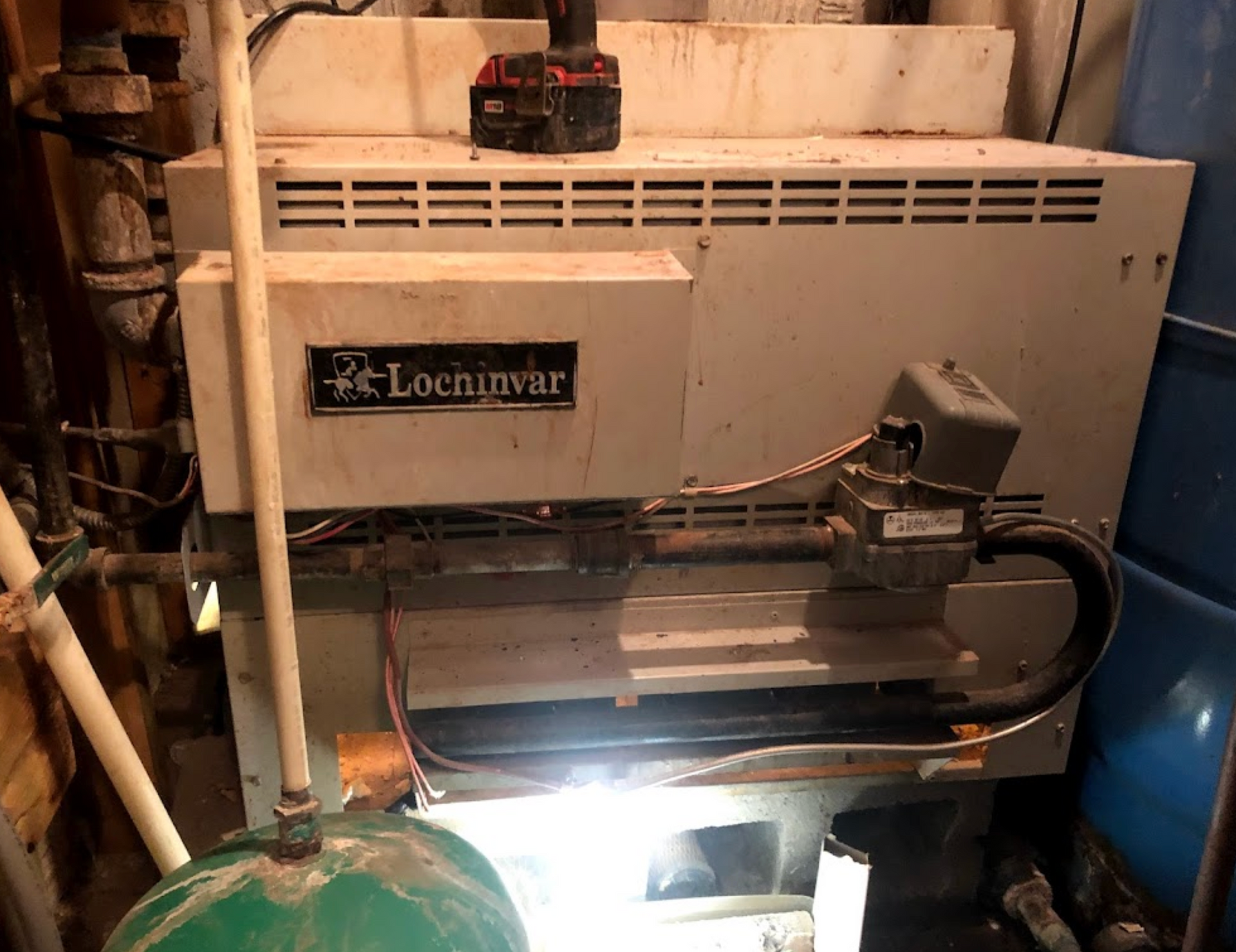 A boiler is sitting in a basement next to a green tank.